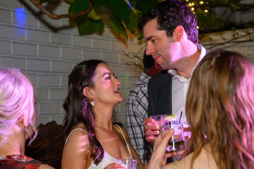 People chatting and smiling at a party, holding drinks in a decorated indoor setting.