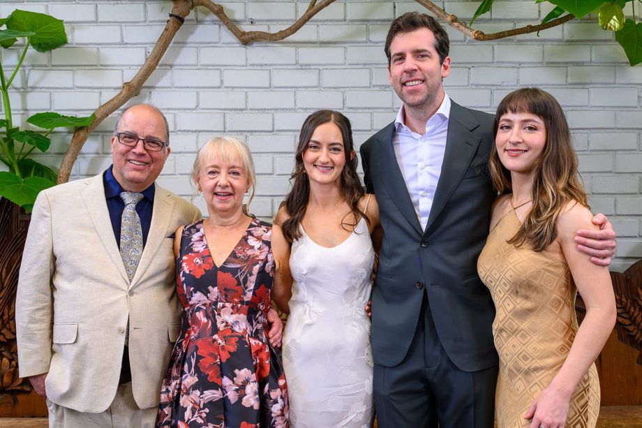 Five people posing together at a formal event, with a brick wall and greenery in the background.
