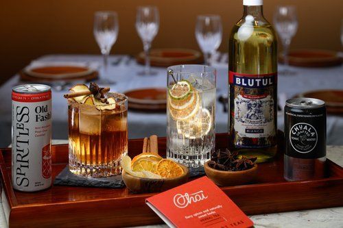 Assorted alcoholic drinks and a soda can on a table with blurred glasses in the background