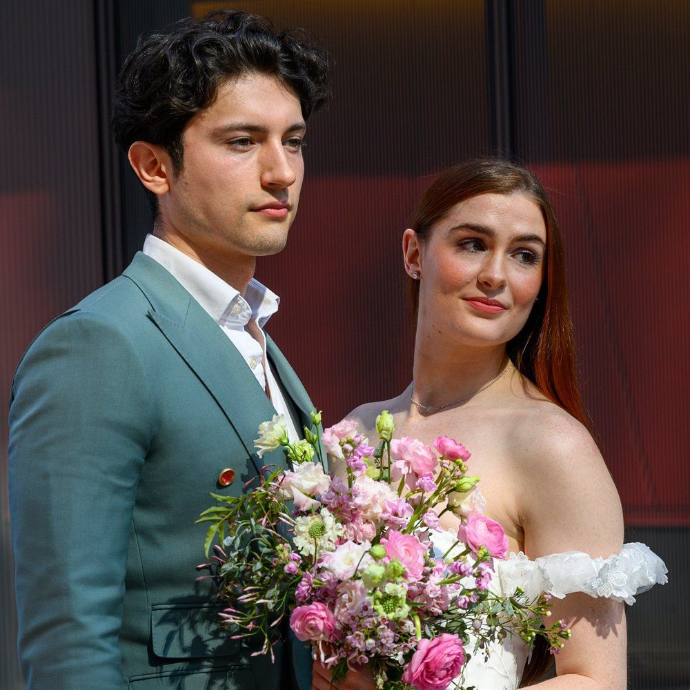 A couple posing at a formal event, holding a large bouquet of pink and white flowers.