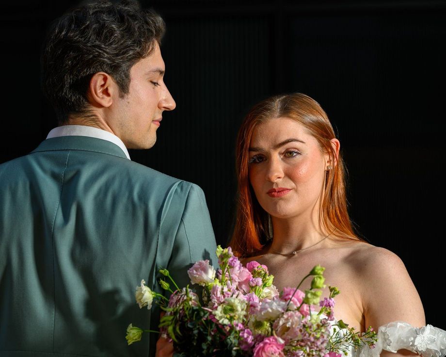 Couple in formal attire posing with a bouquet against a dark background