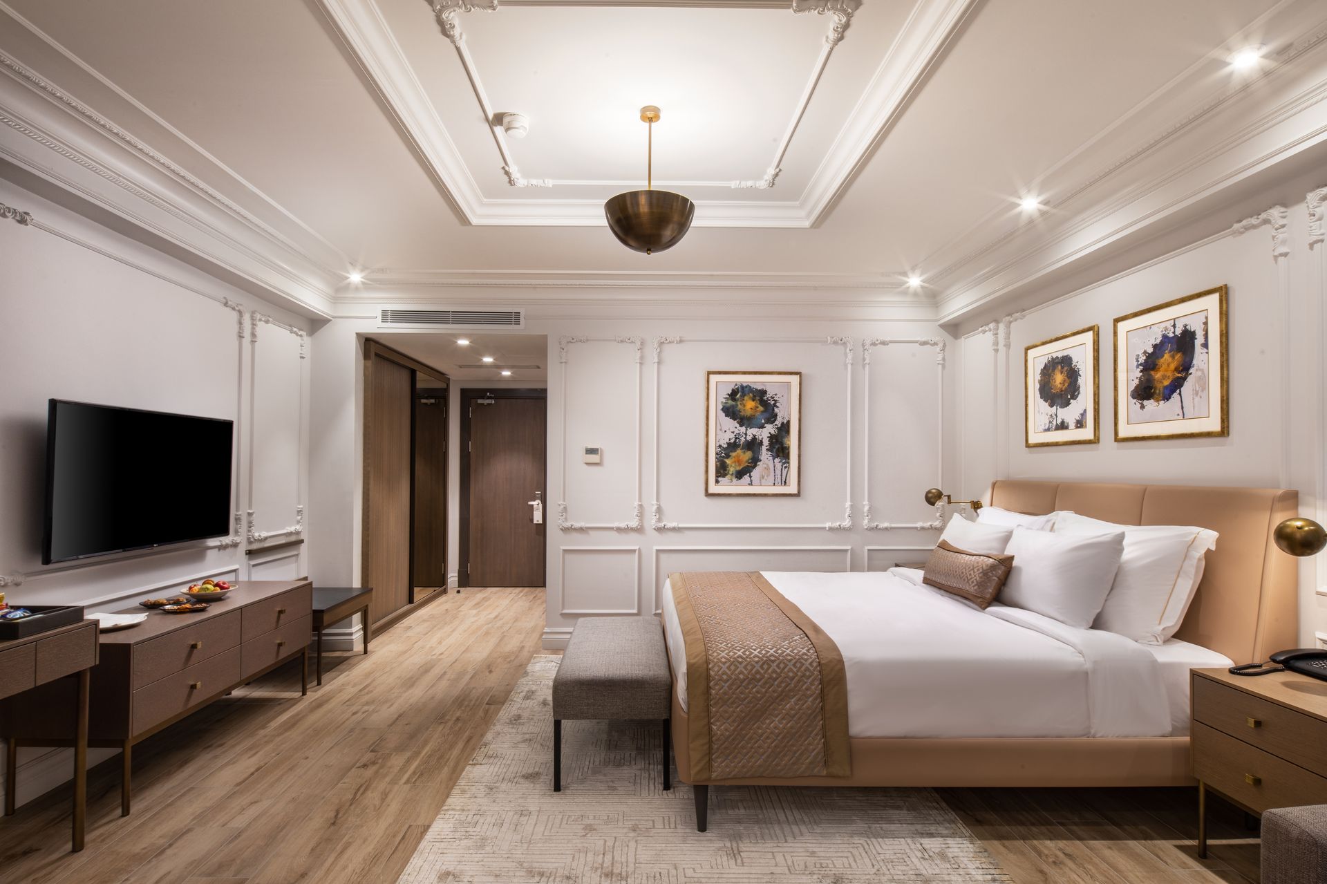 Elegant hotel bedroom with king bed, TV, desk, and warm white decor