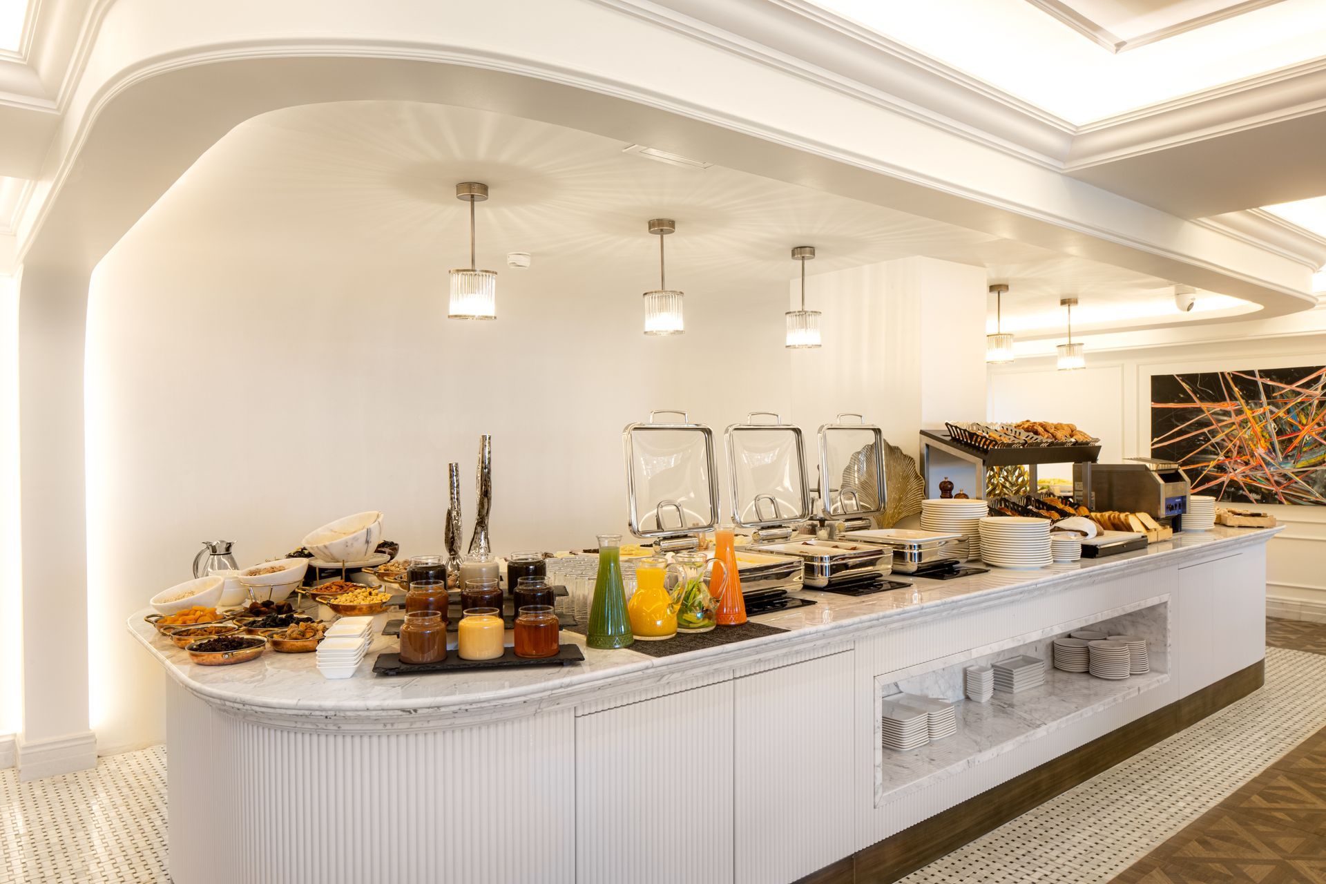 Elegant hotel buffet with pastries, fruit, drinks, and glassware under a bright arched ceiling