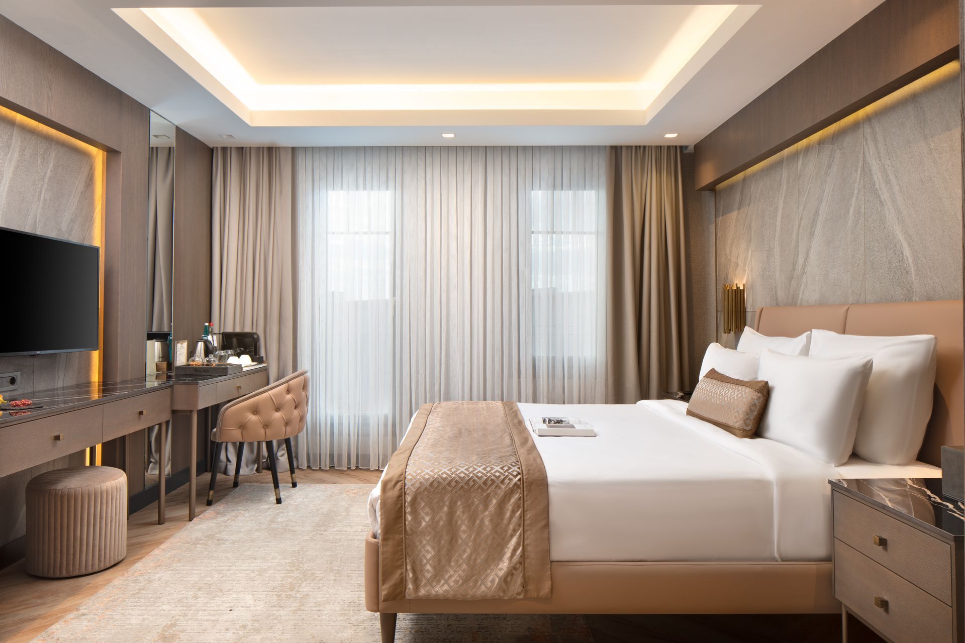 Modern hotel room with a bed, desk, TV, and large curtains by a window | Mula Hotel
