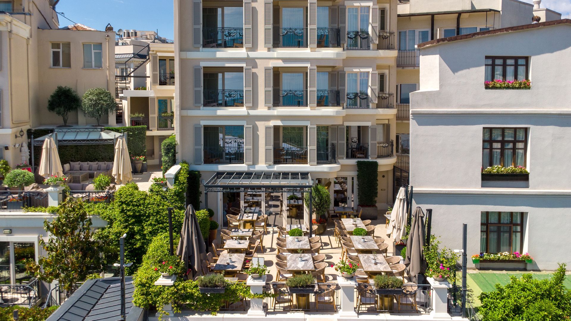 Modern hotel courtyard with outdoor dining tables, umbrellas, and balconies in bright sunlight