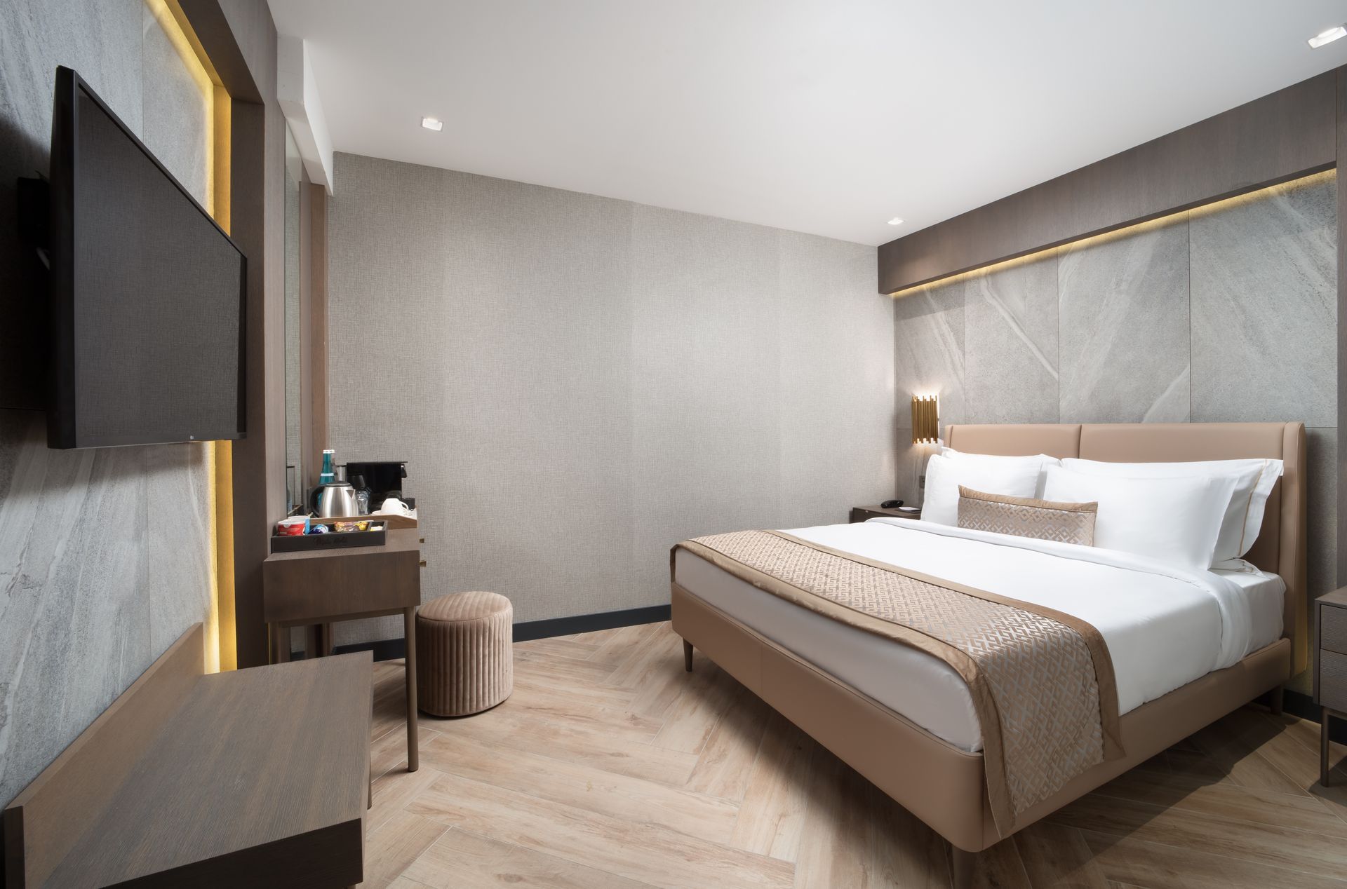 Modern hotel room with a neatly made bed, wall-mounted TV, and a small desk in neutral gray tones