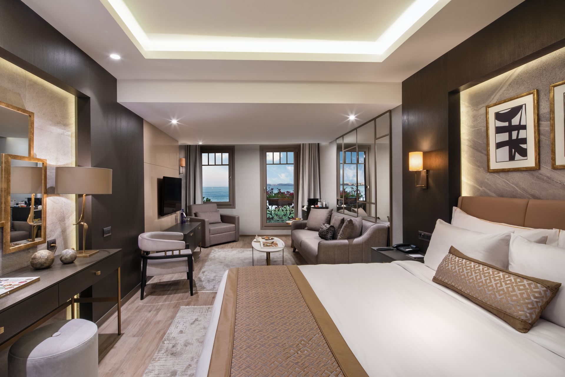 Modern hotel bedroom with a large bed, seating area, and city view through floor-to-ceiling windows