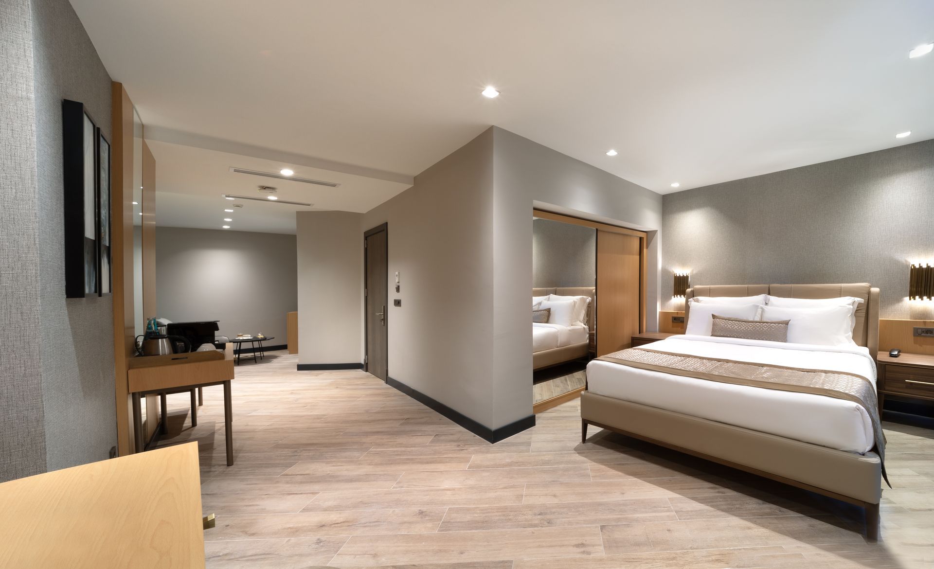Modern hotel suite with a large bed, desk, and open living area in neutral tones