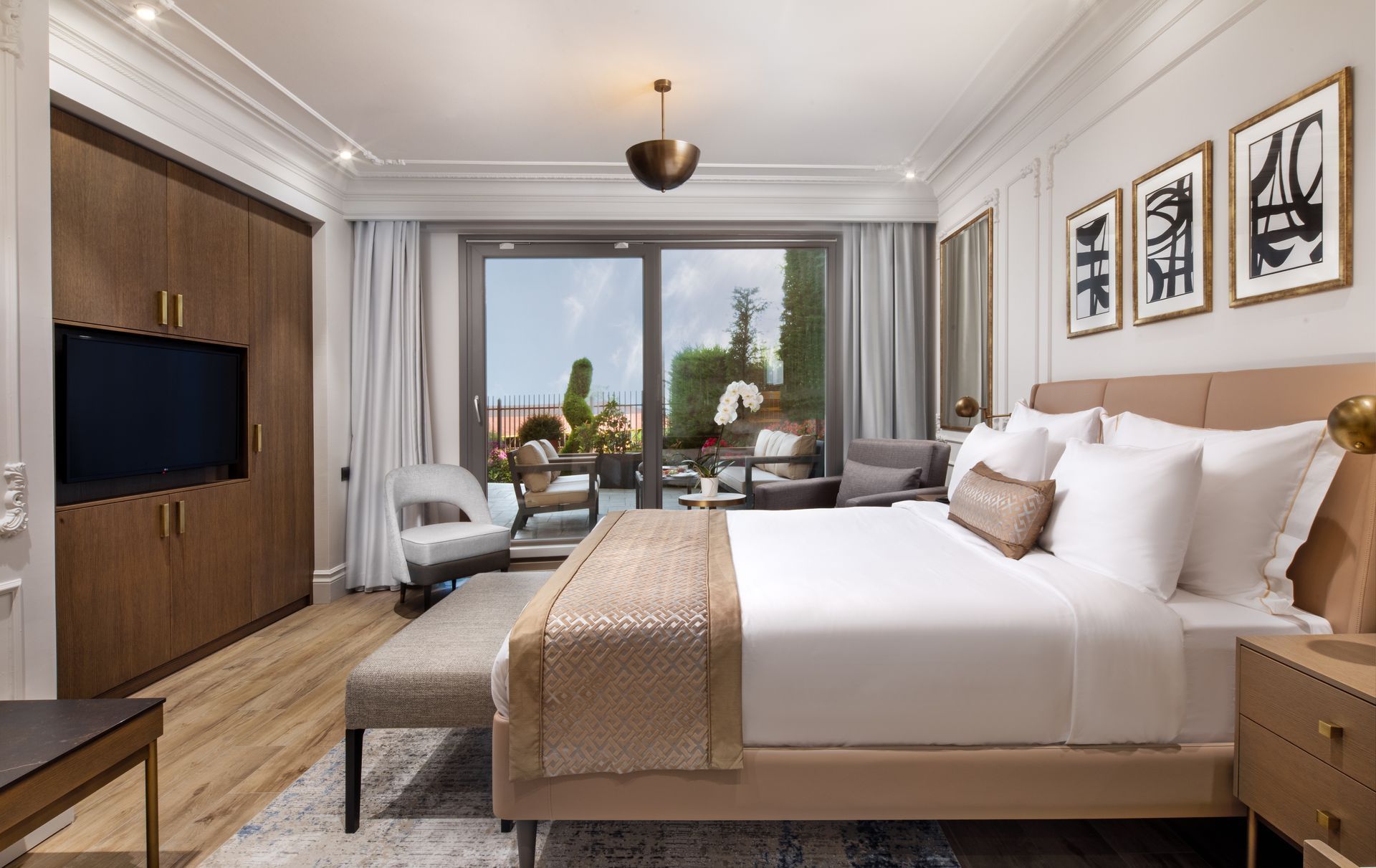Modern hotel room with king bed, lounge chair, desk, TV, and balcony view of the city.