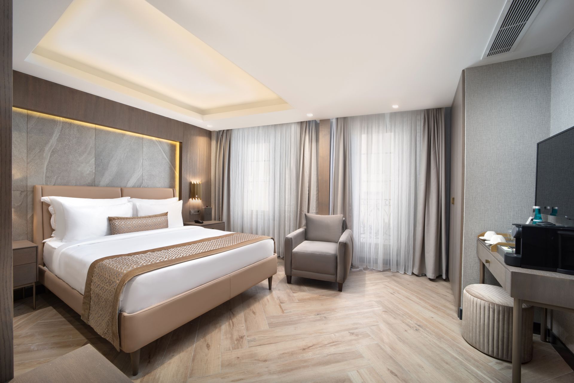 Modern hotel bedroom with a king bed, gray armchair, curtains, and soft neutral decor | Mula Hotel