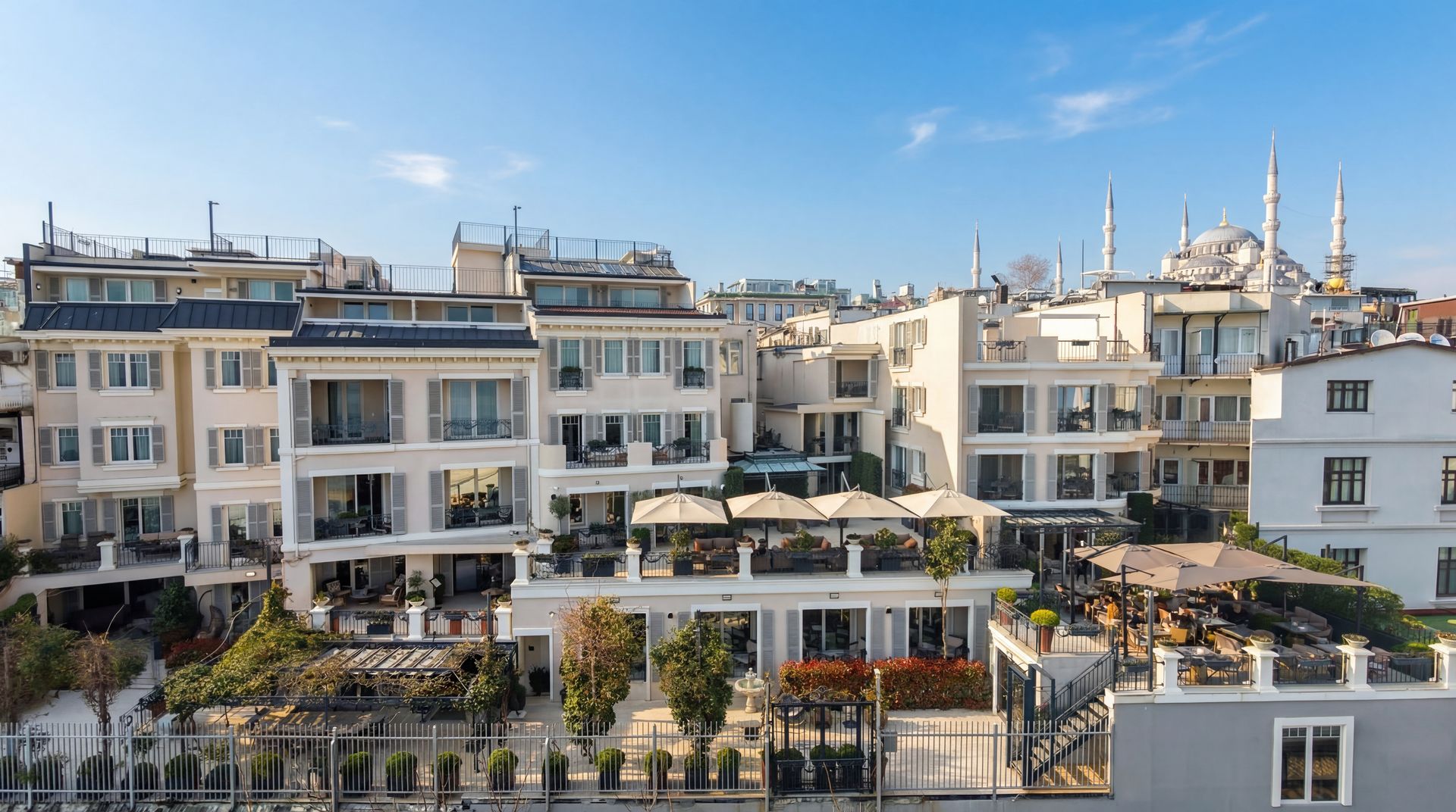 Bright waterfront buildings with rooftop terraces under a blue sky, likely a seaside resort or cityscape