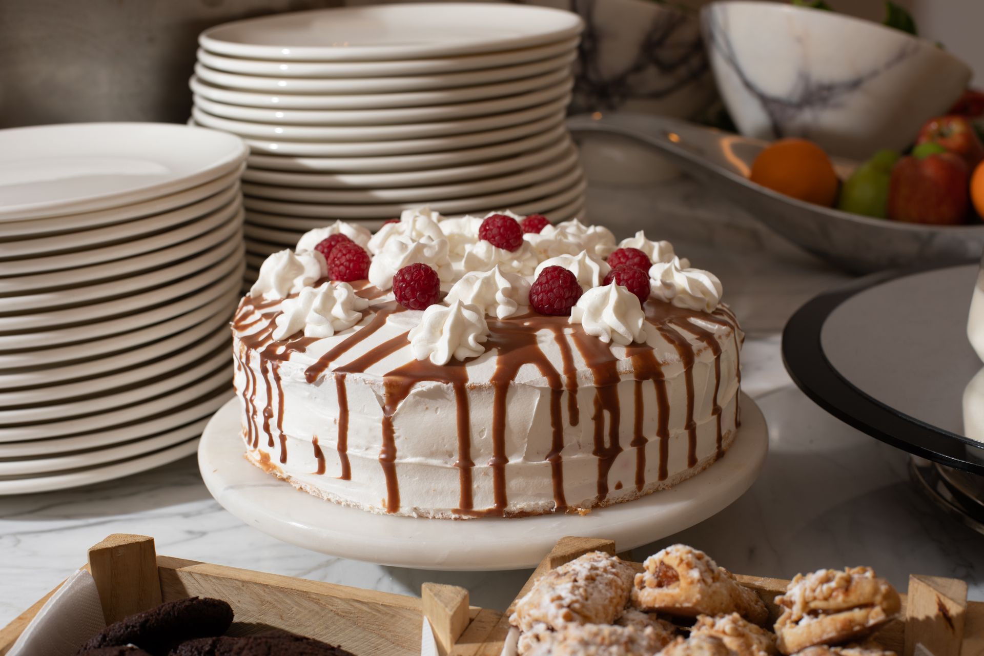 White frosted cake with strawberries and raspberries on a buffet table beside stacked plates