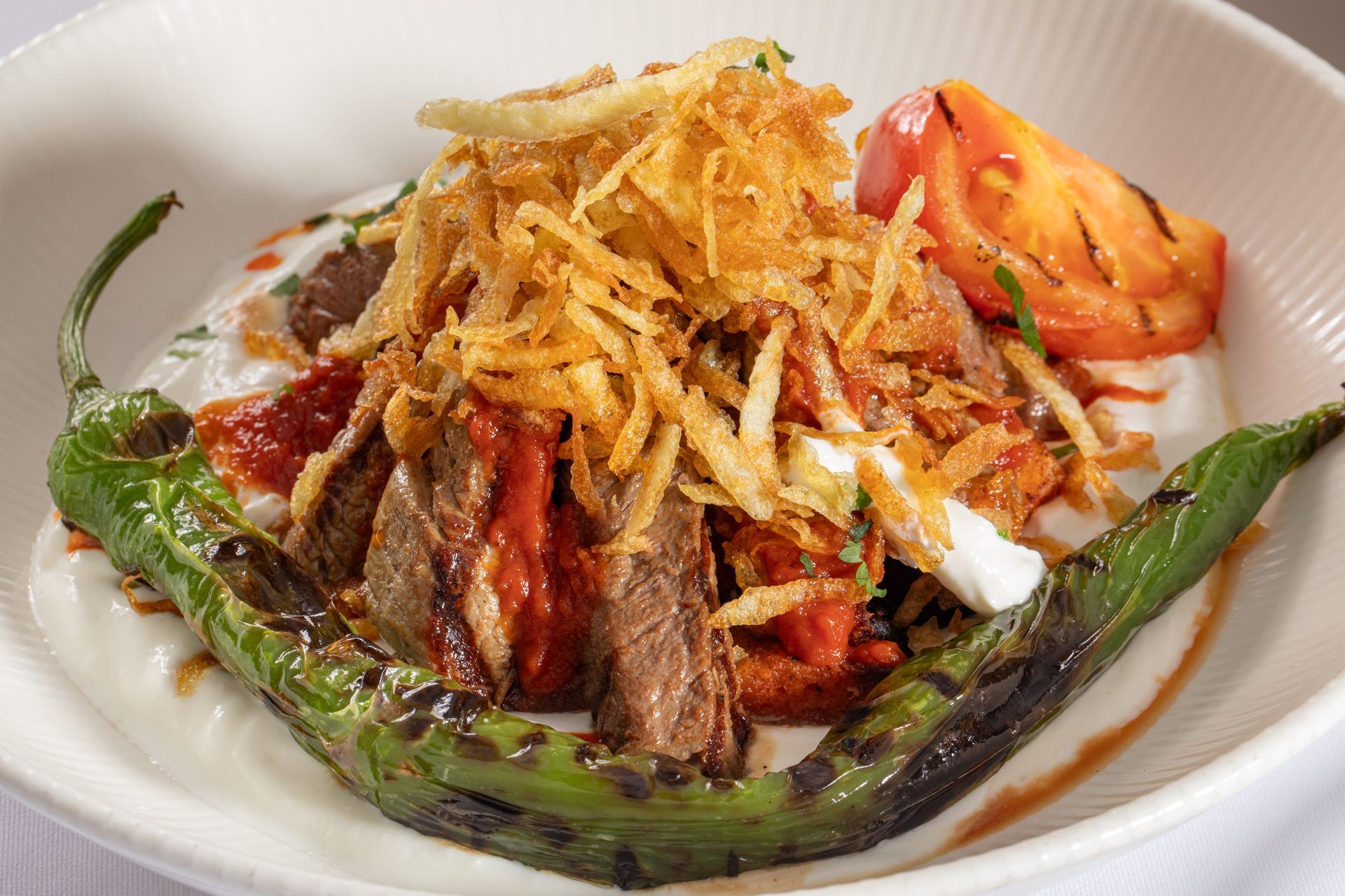 Plated salad with grilled vegetables, tomatoes, and crispy fried onions on a white dish