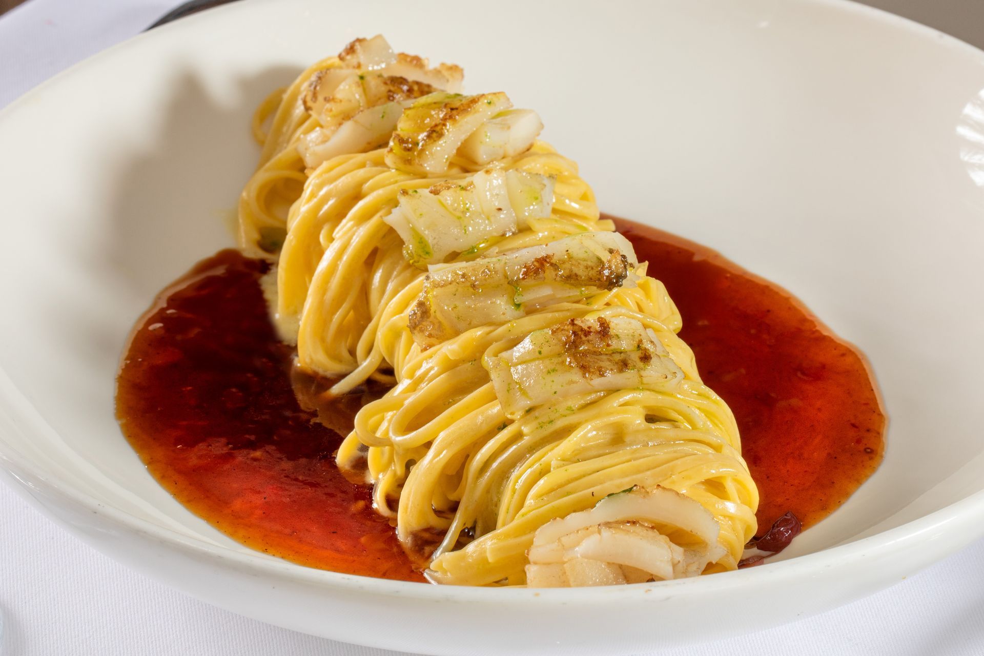 Plated seafood cannelloni with creamy sauce on a red tomato coulis