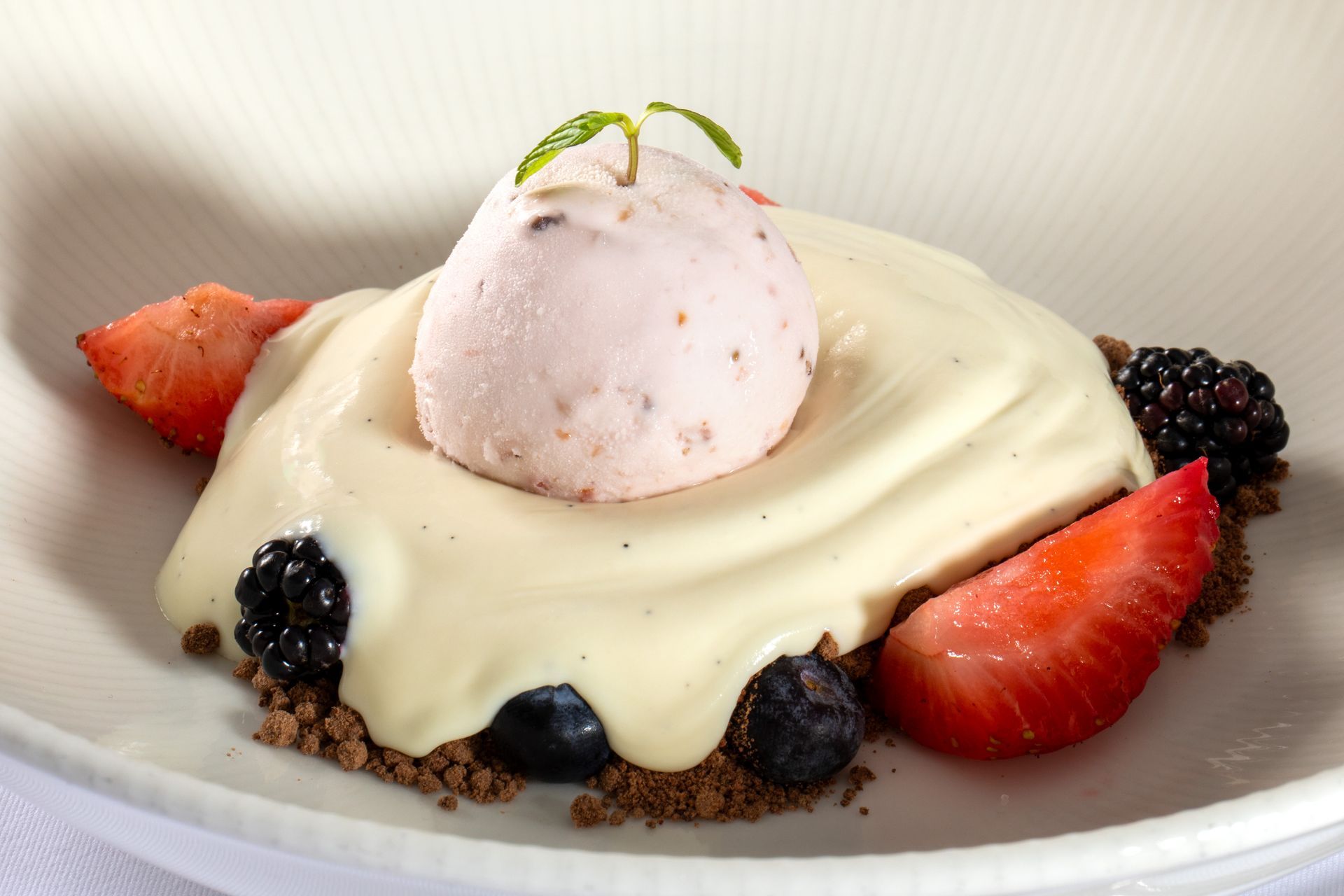 Dessert plate with cream-covered cake, strawberry, blackberries, and a scoop of ice cream topped with lime zest