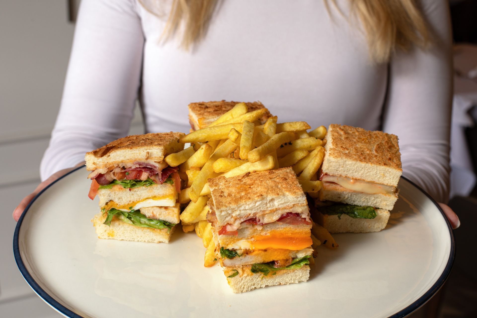 Sandwiches and French fries on a plate held by a person in a white shirt