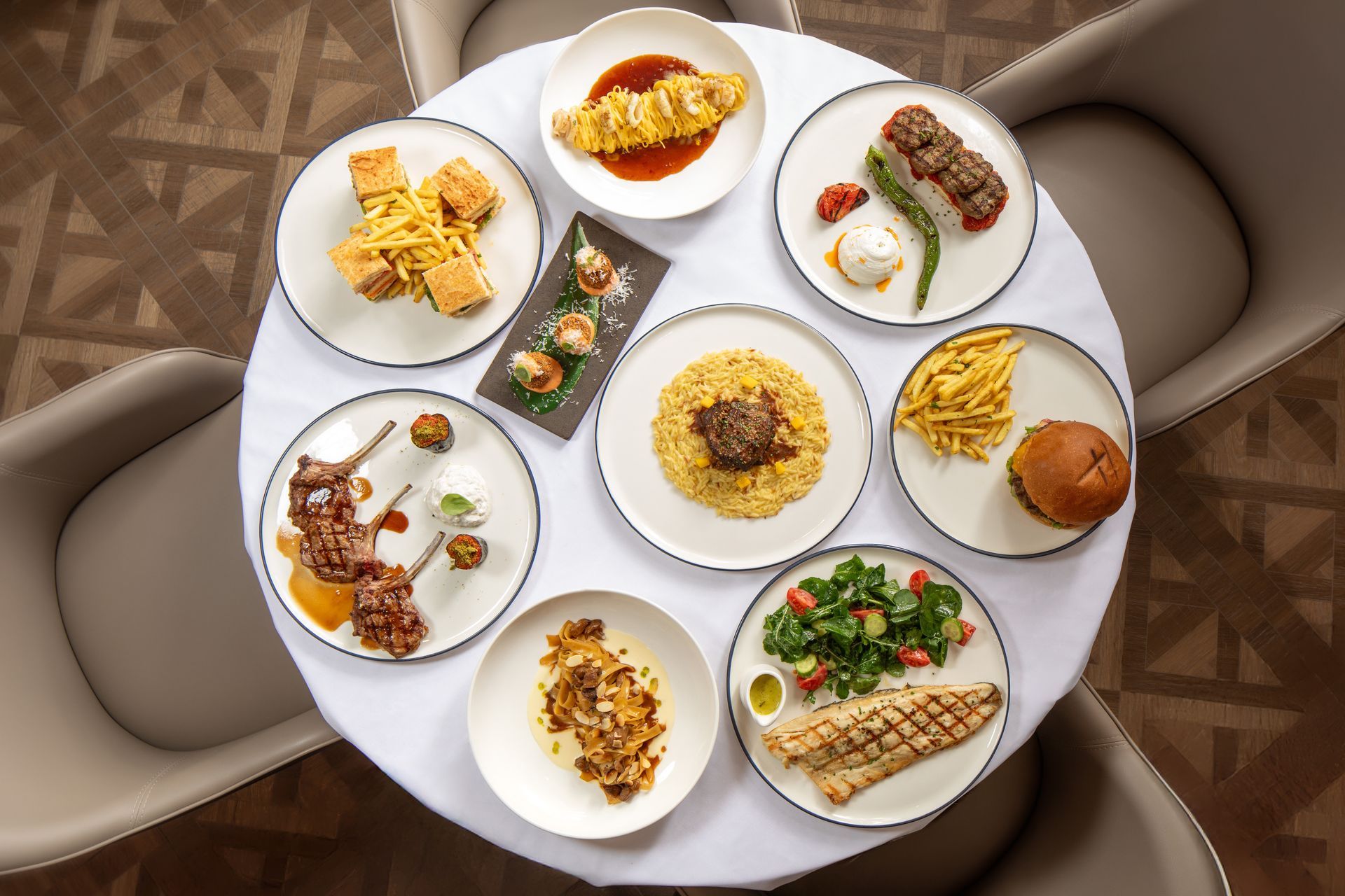 Assorted plated dishes arranged on a round white dining table in a modern lounge.