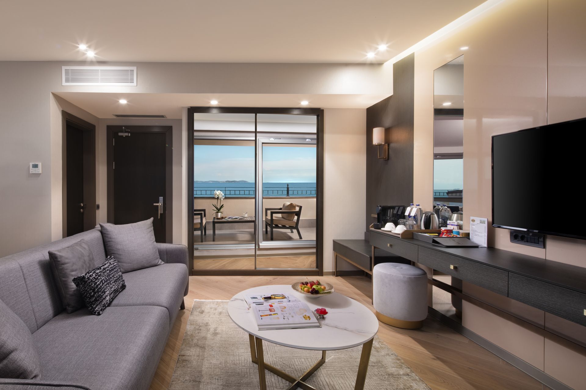 Modern living room with sofa, TV, coffee table, and ocean-view balcony beyond glass doors