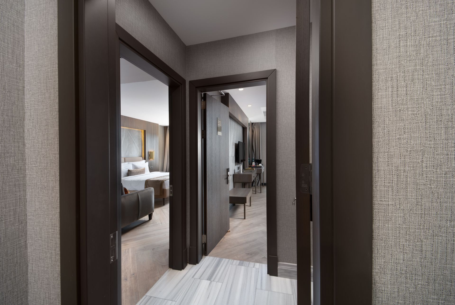 Modern apartment hallway with dark wood doorframes and a bedroom visible at the end.