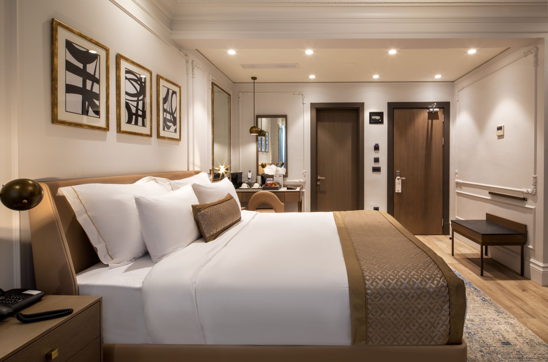 Modern hotel room with a king bed, warm wood accents, desk, mirror, and framed wall art