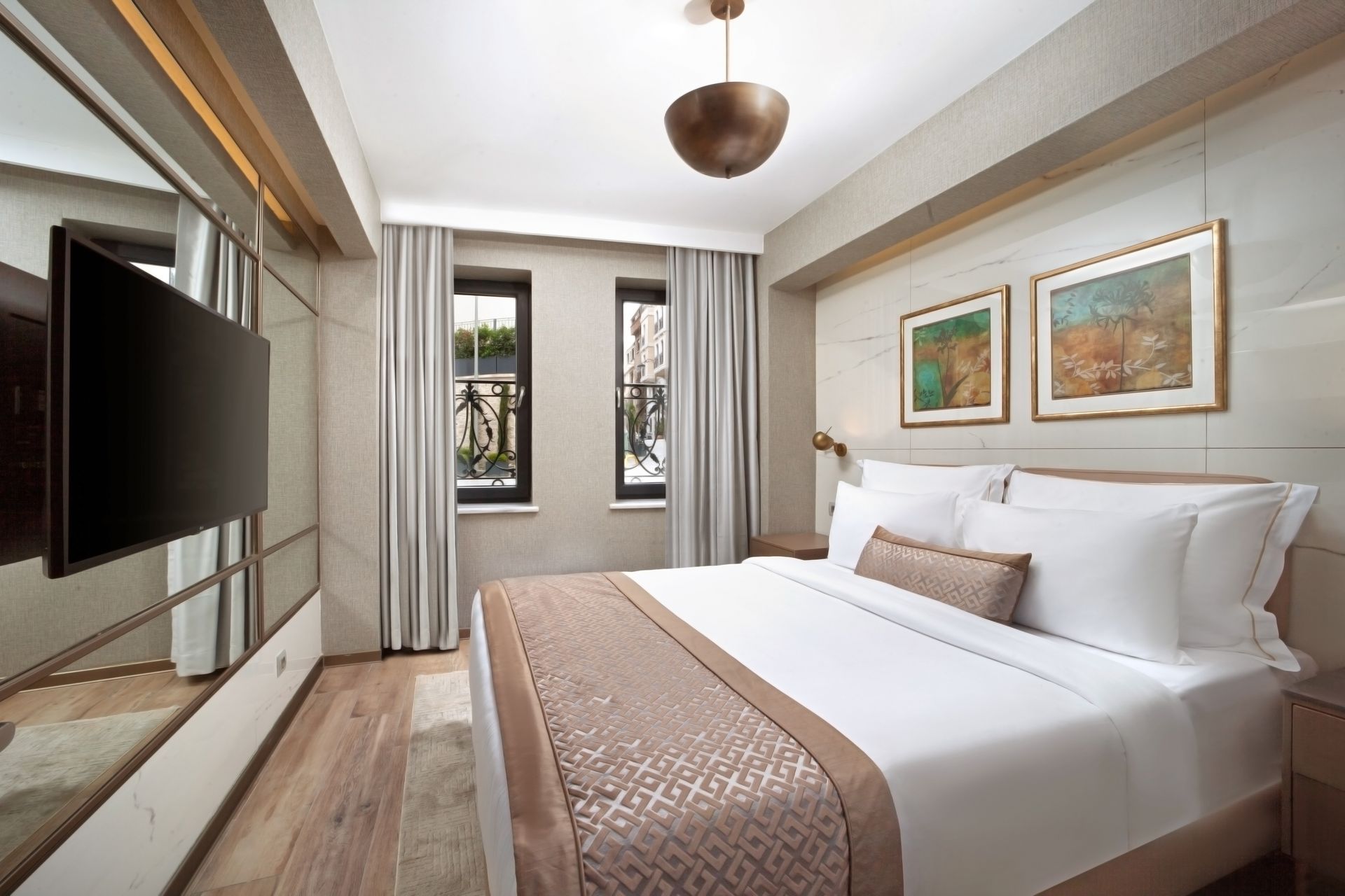 Modern bedroom with a large bed, wall-mounted TV, and two framed artworks by a window