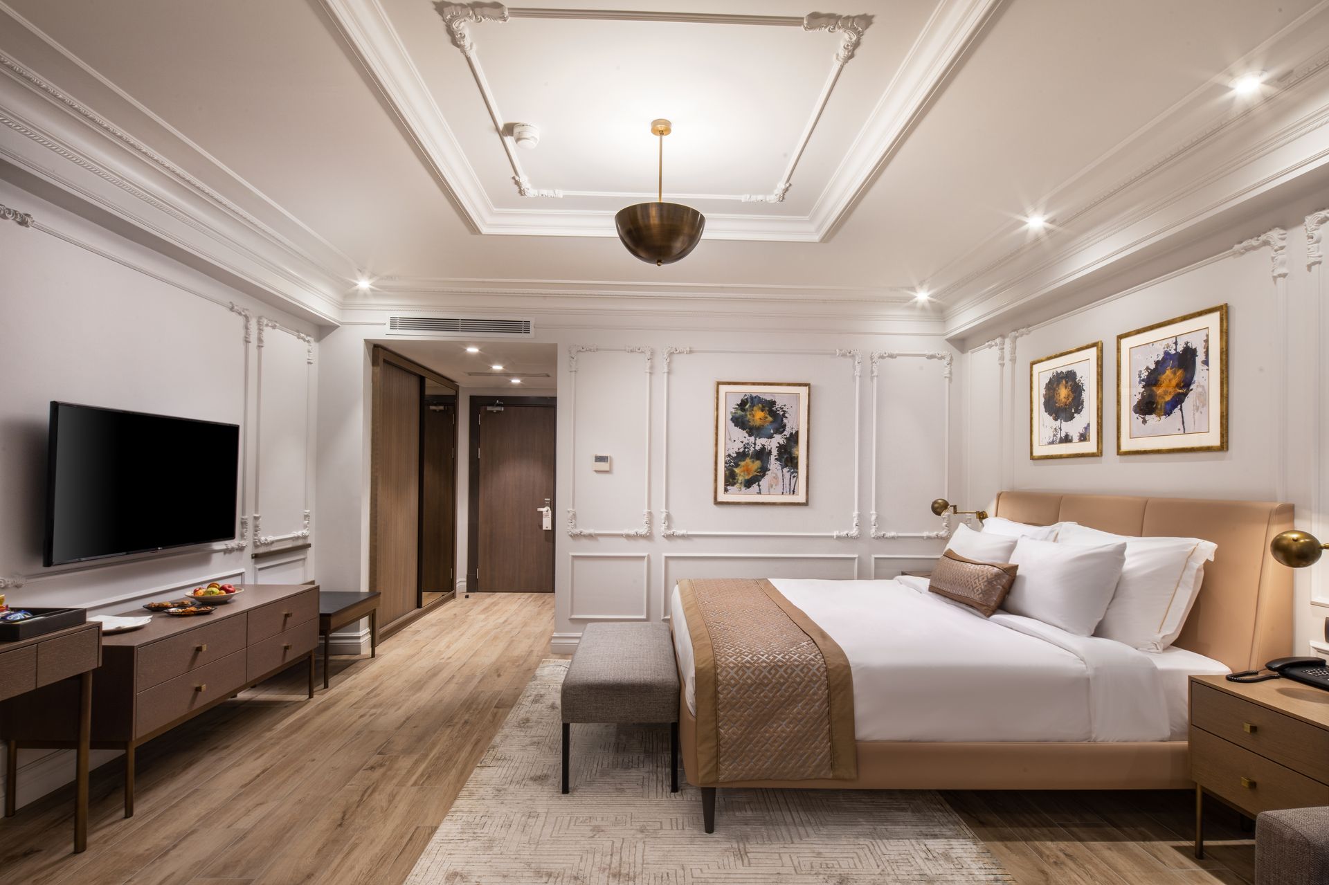 Elegant hotel bedroom with a king bed, TV, desk, and warm beige decor