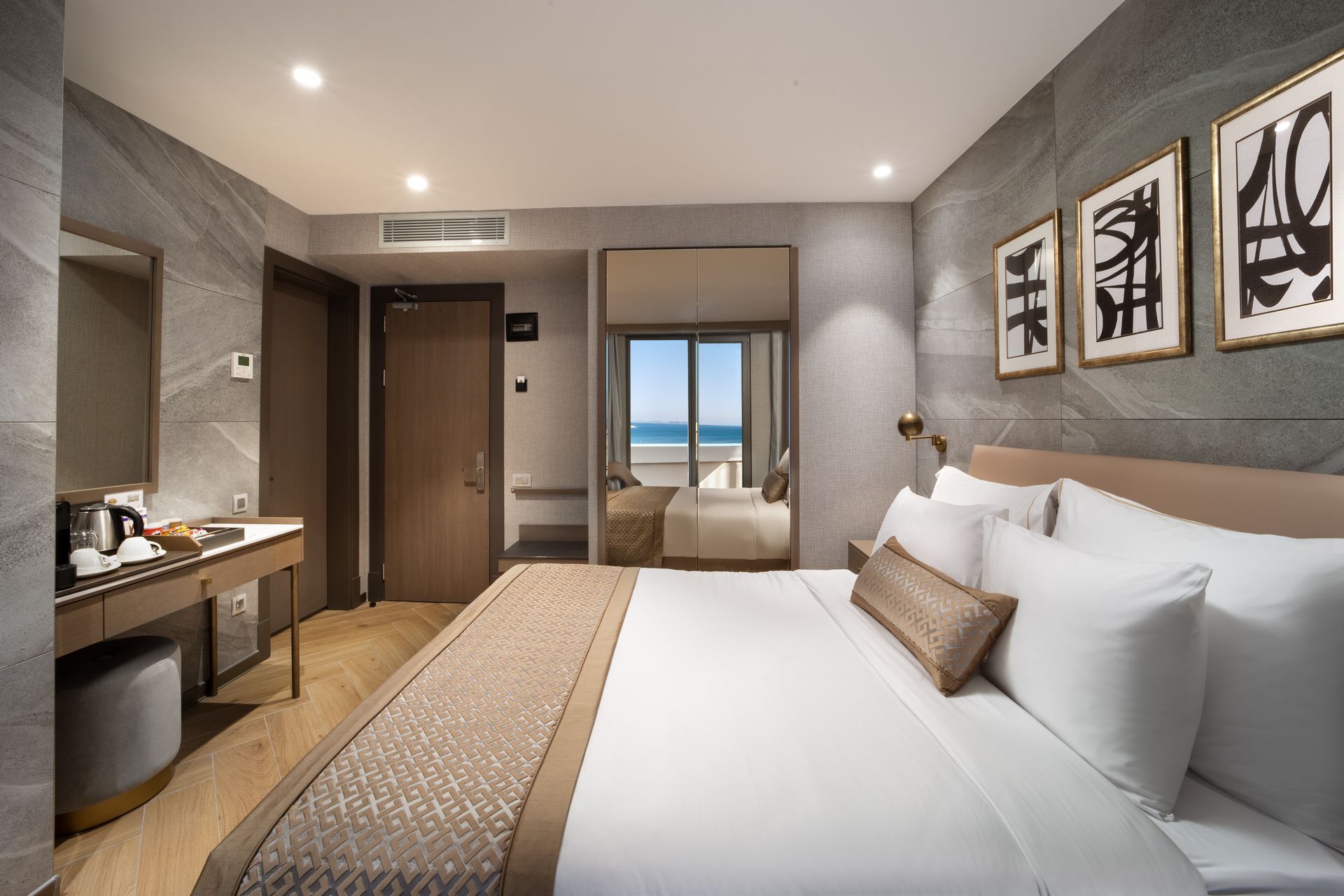 Modern hotel room with a large bed, desk, wall art, and a view through the window