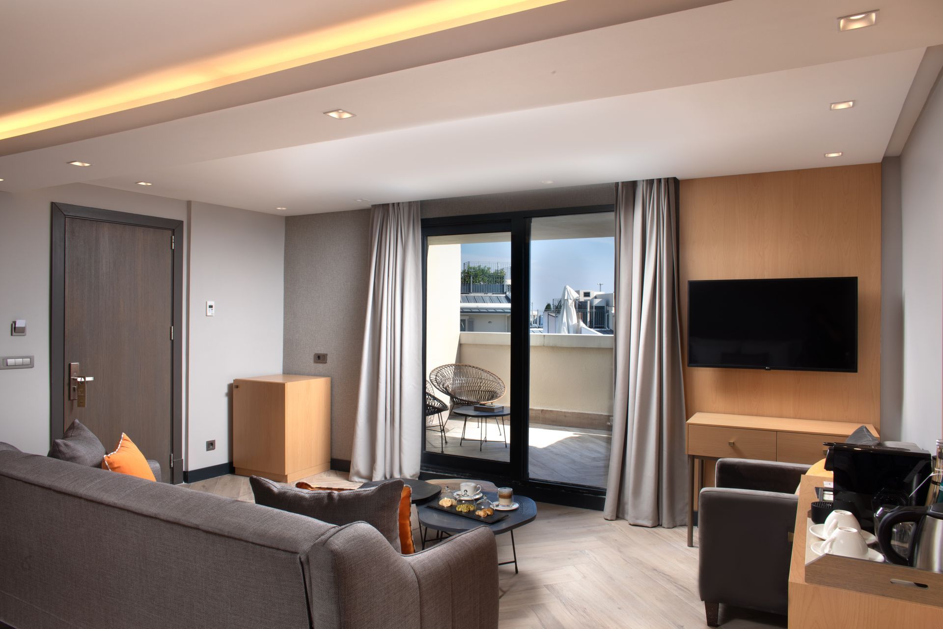 Modern living room with gray sofa, TV, wood accents, and balcony doors overlooking the water