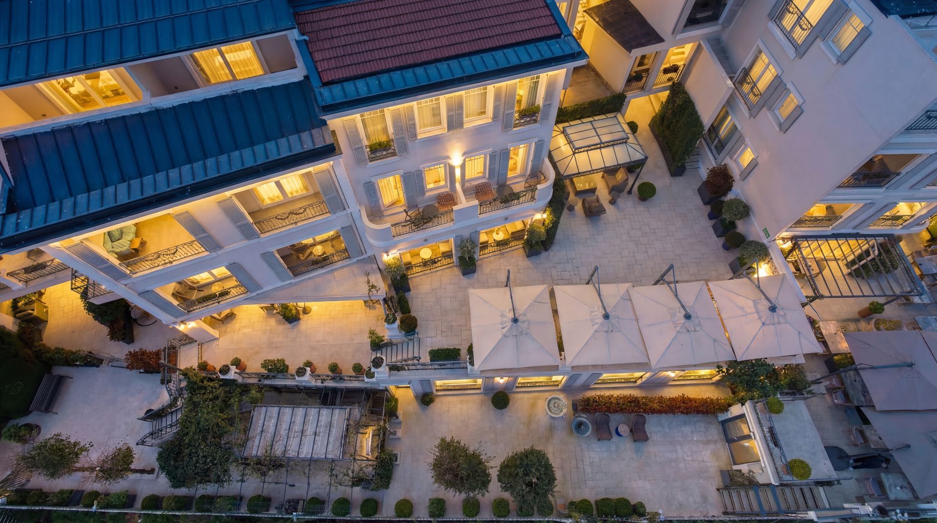 Aerial view of a courtyard with outdoor seating, warm-lit buildings, and umbrellas at dusk.