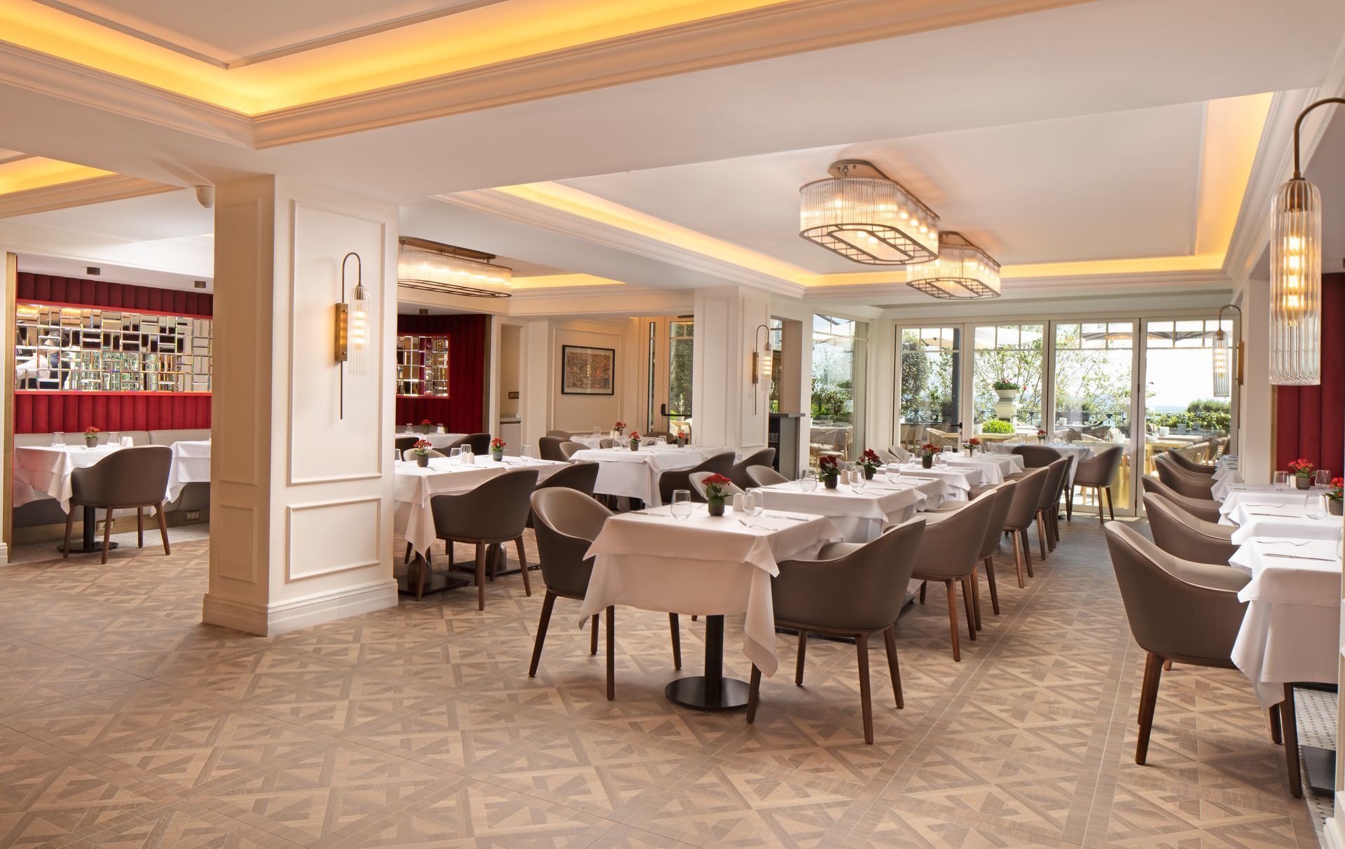 Elegant hotel dining room with set tables, chandeliers, and large windows overlooking greenery