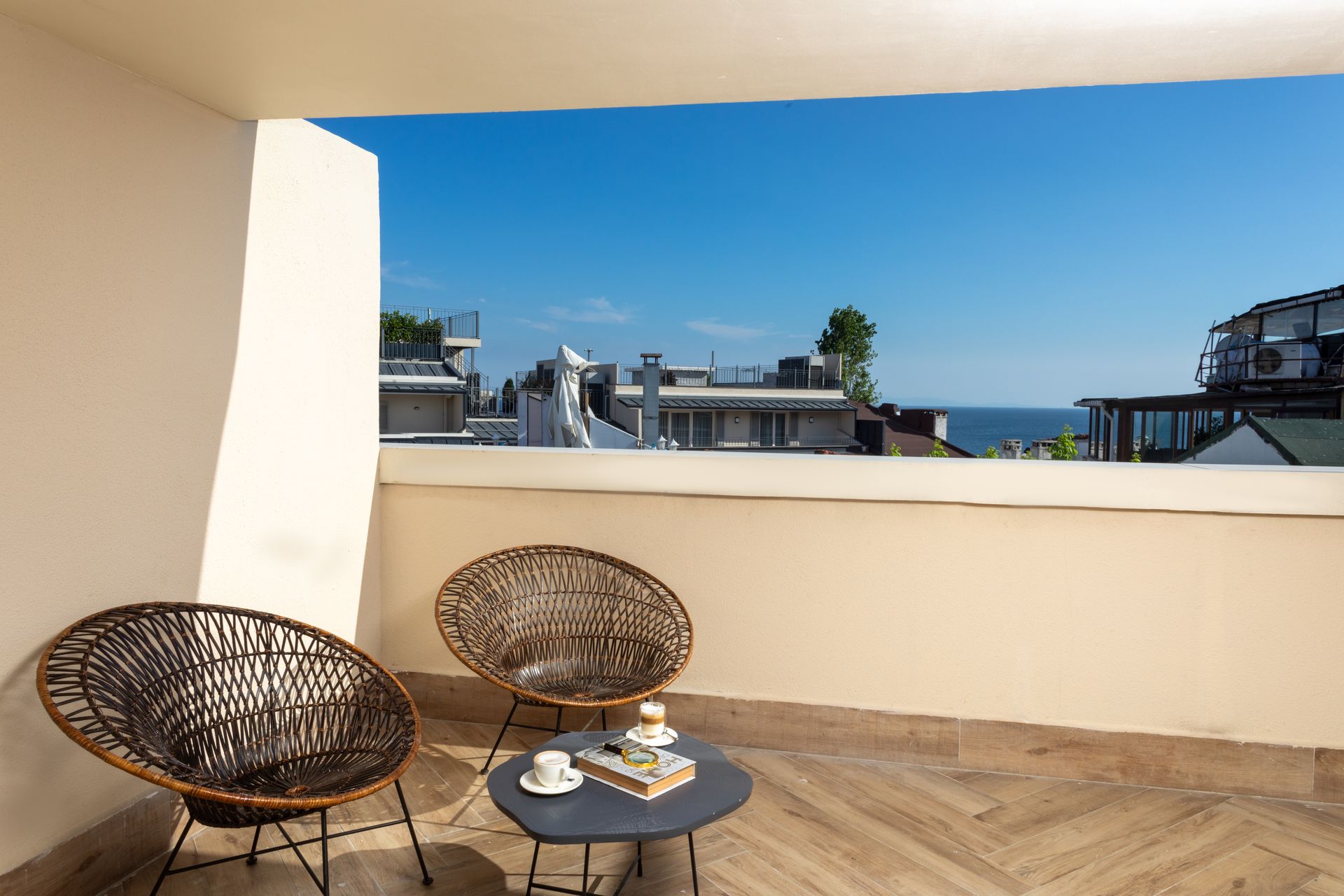 Terrace with two woven chairs, small table, and ocean view under a clear blue sky