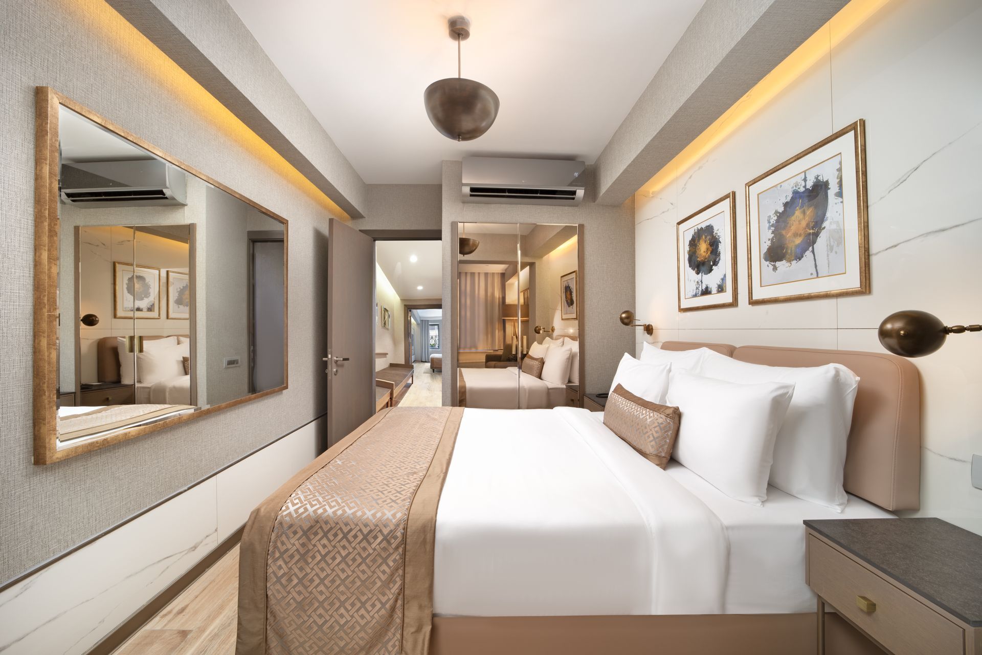Modern hotel bedroom with a king bed, mirrored wall, warm lighting, and framed artwork