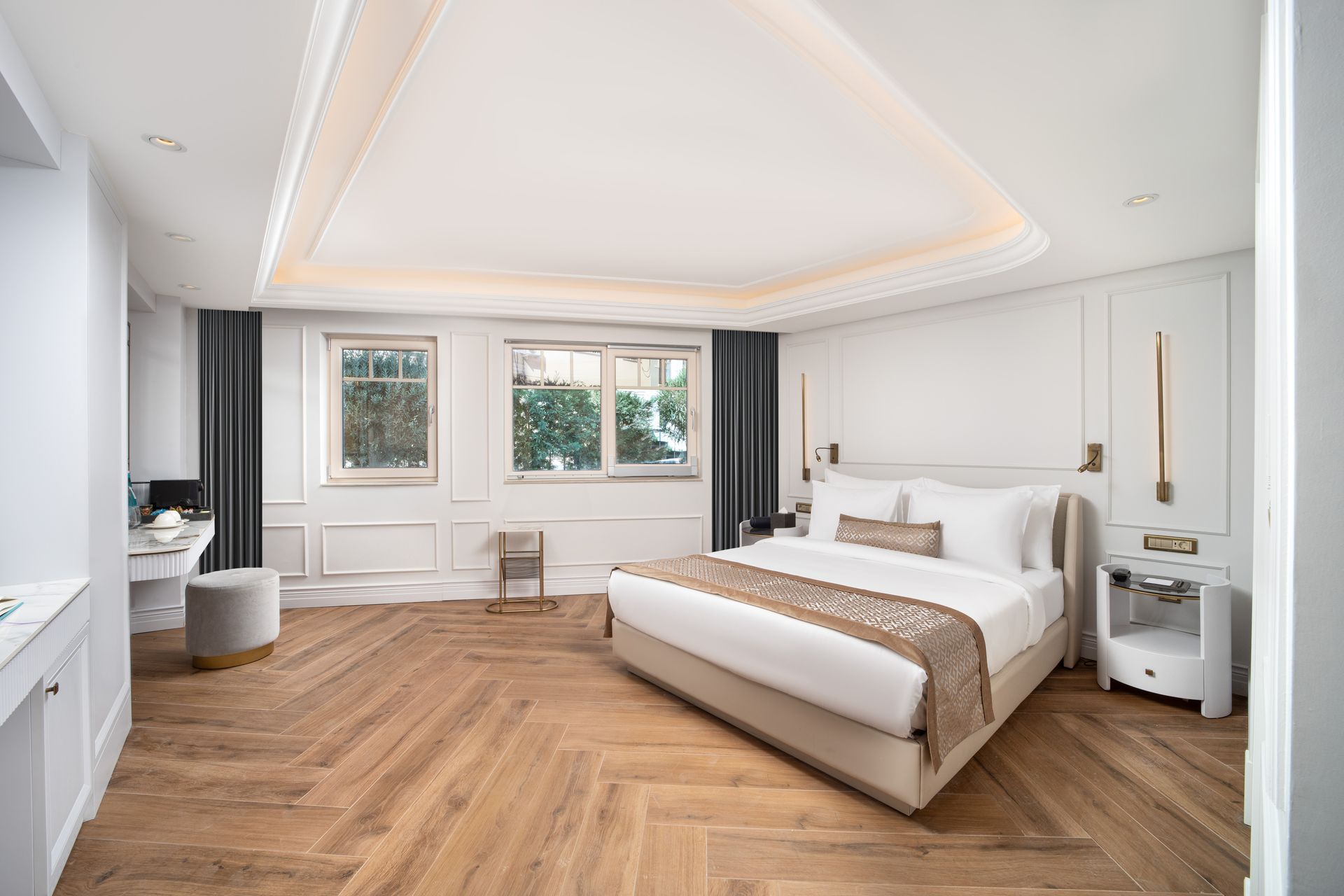 Bright, modern bedroom with a white bed, herringbone wood floor, and large windows.