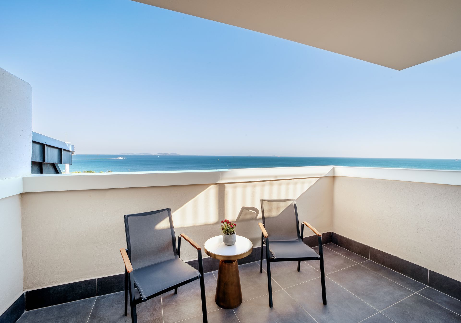Balcony with two chairs and a small table overlooking the ocean and blue sky
