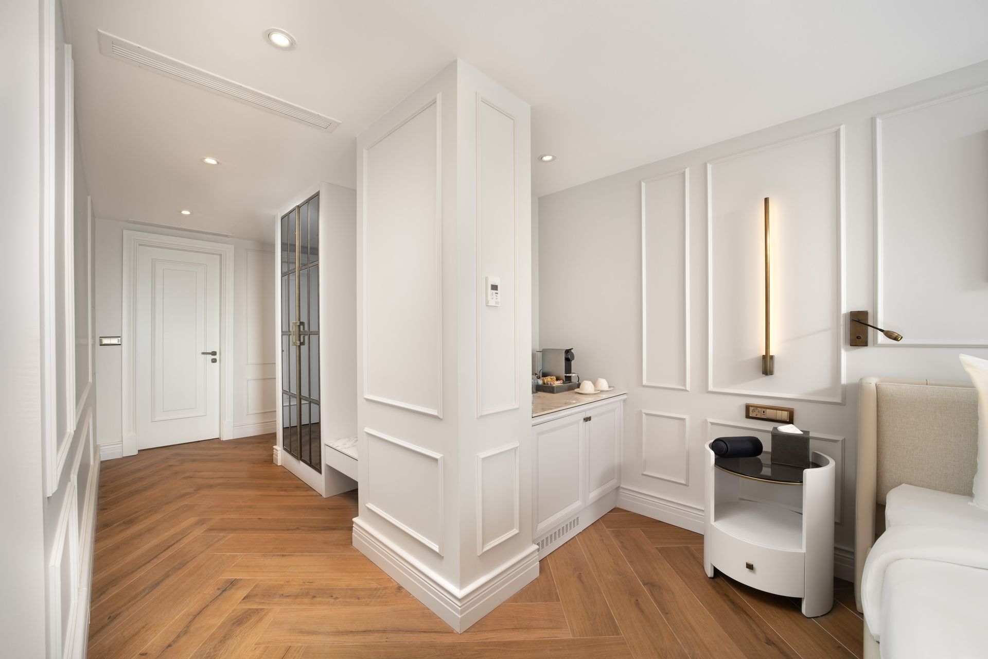 Bright hallway with herringbone wood floor, white paneled walls, mirror, vanity, and beige sofa seating area