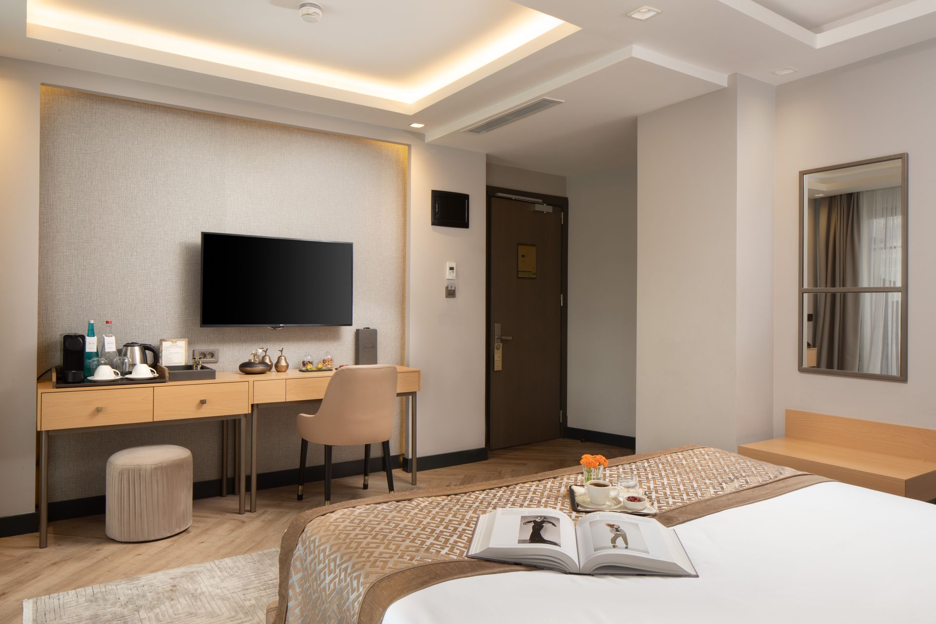 Modern hotel room with bed, desk, TV, and beige decor