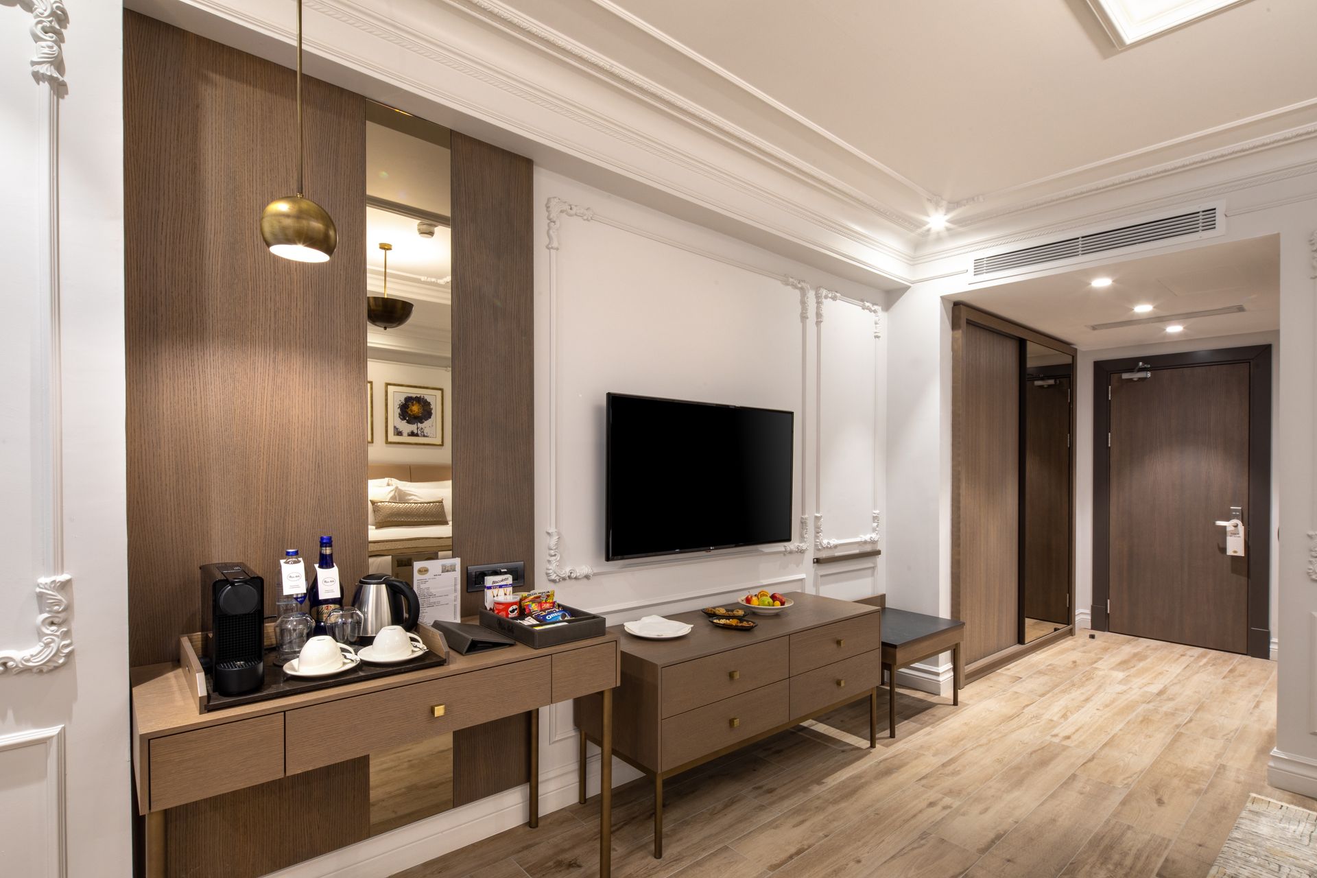 Modern hotel room with two beds, TV, vanity desk, and warm wood-paneled walls