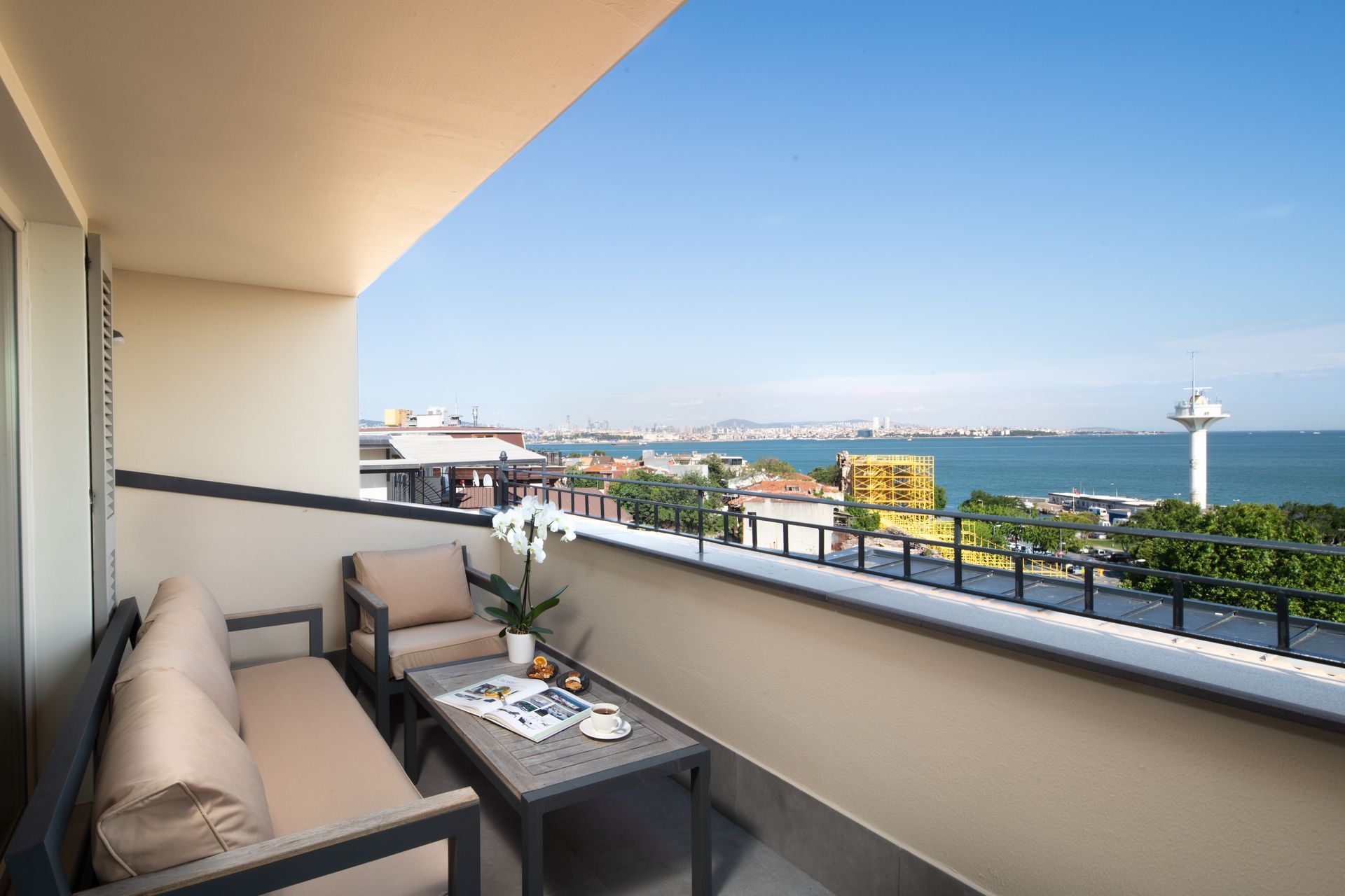 Balcony with sofa and table overlooking a seaside harbor and blue water at sunset