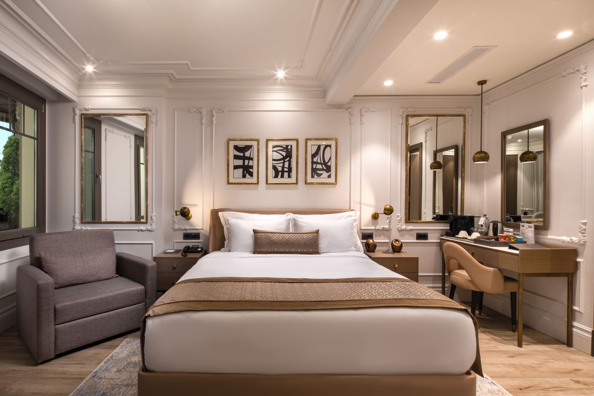 Elegant hotel bedroom with a king bed, gray chair, vanity desk, and warm neutral decor