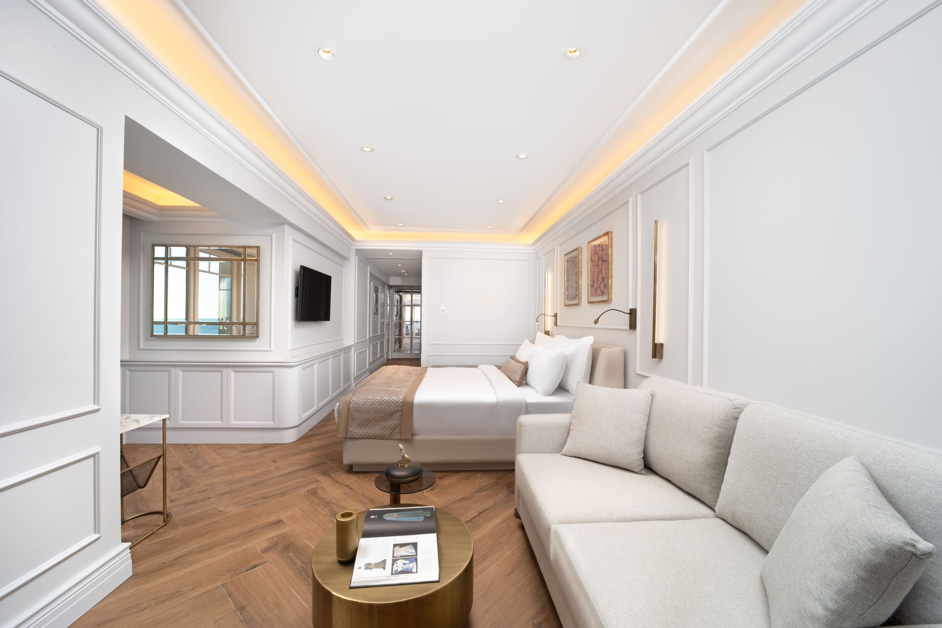 Bright modern bedroom with white walls, beige sofa, bed, and warm recessed lighting