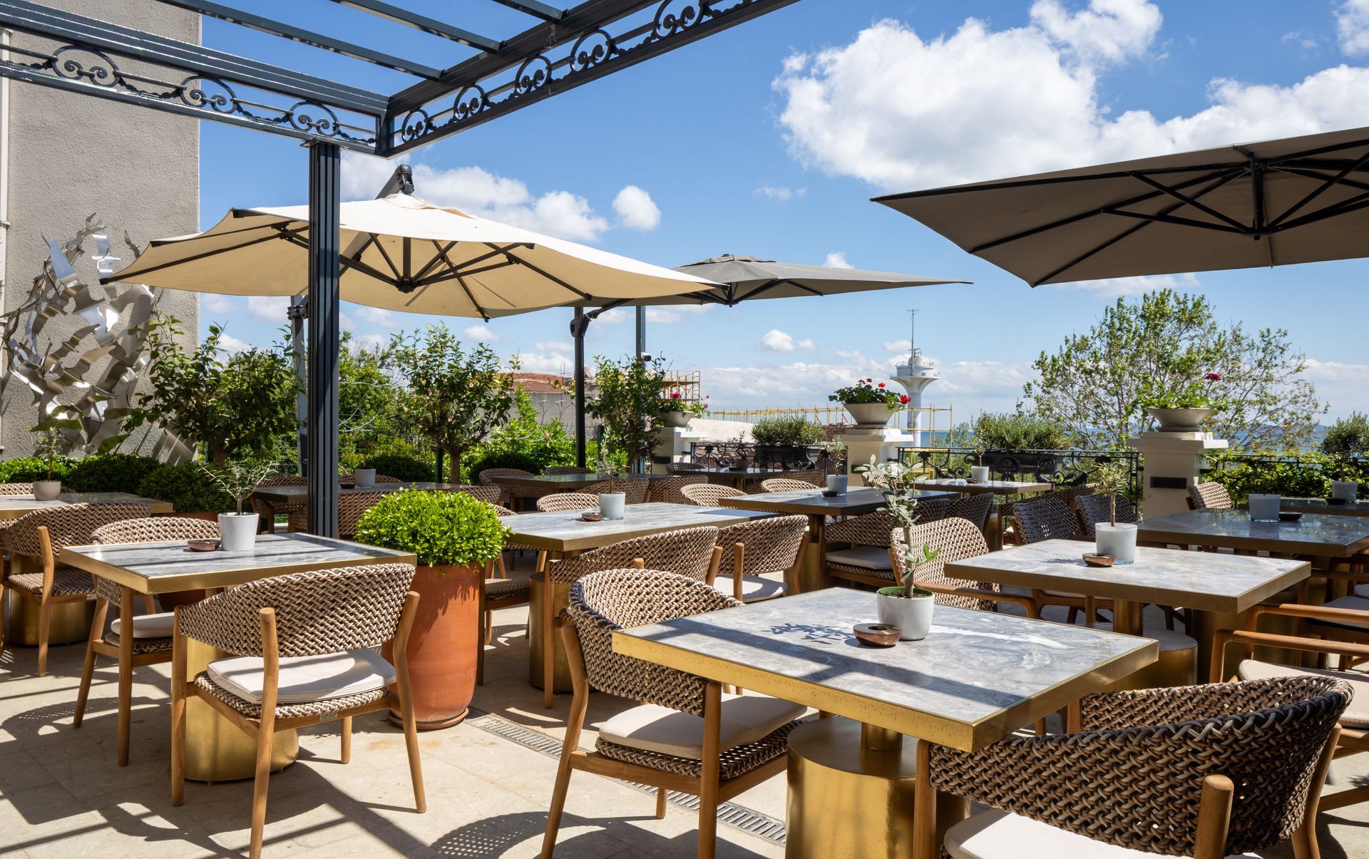 Outdoor rooftop restaurant seating with tables, wicker chairs, umbrellas, and blue sky views