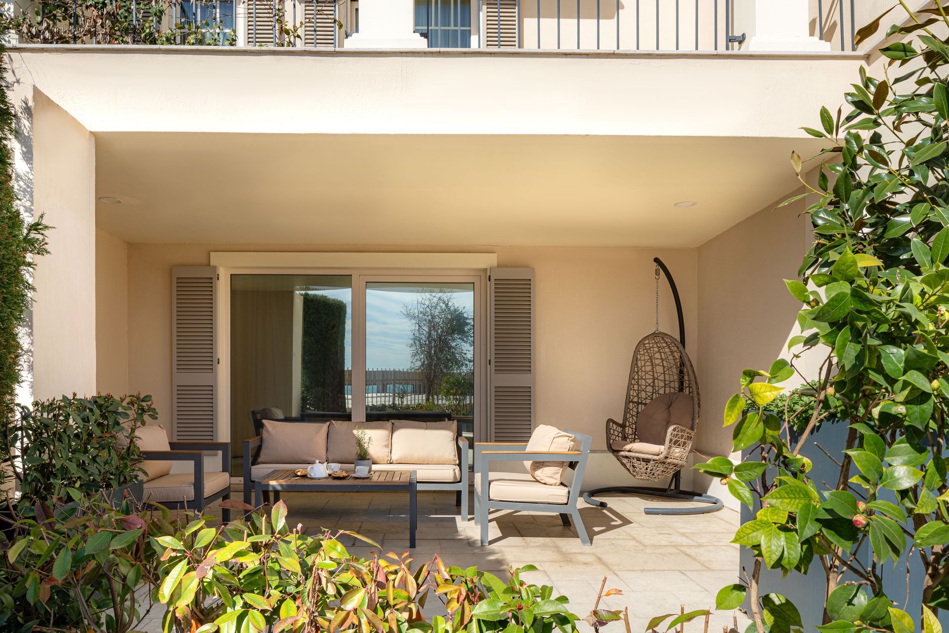 Covered patio with outdoor seating, wicker chair, and greenery in front of sliding glass doors