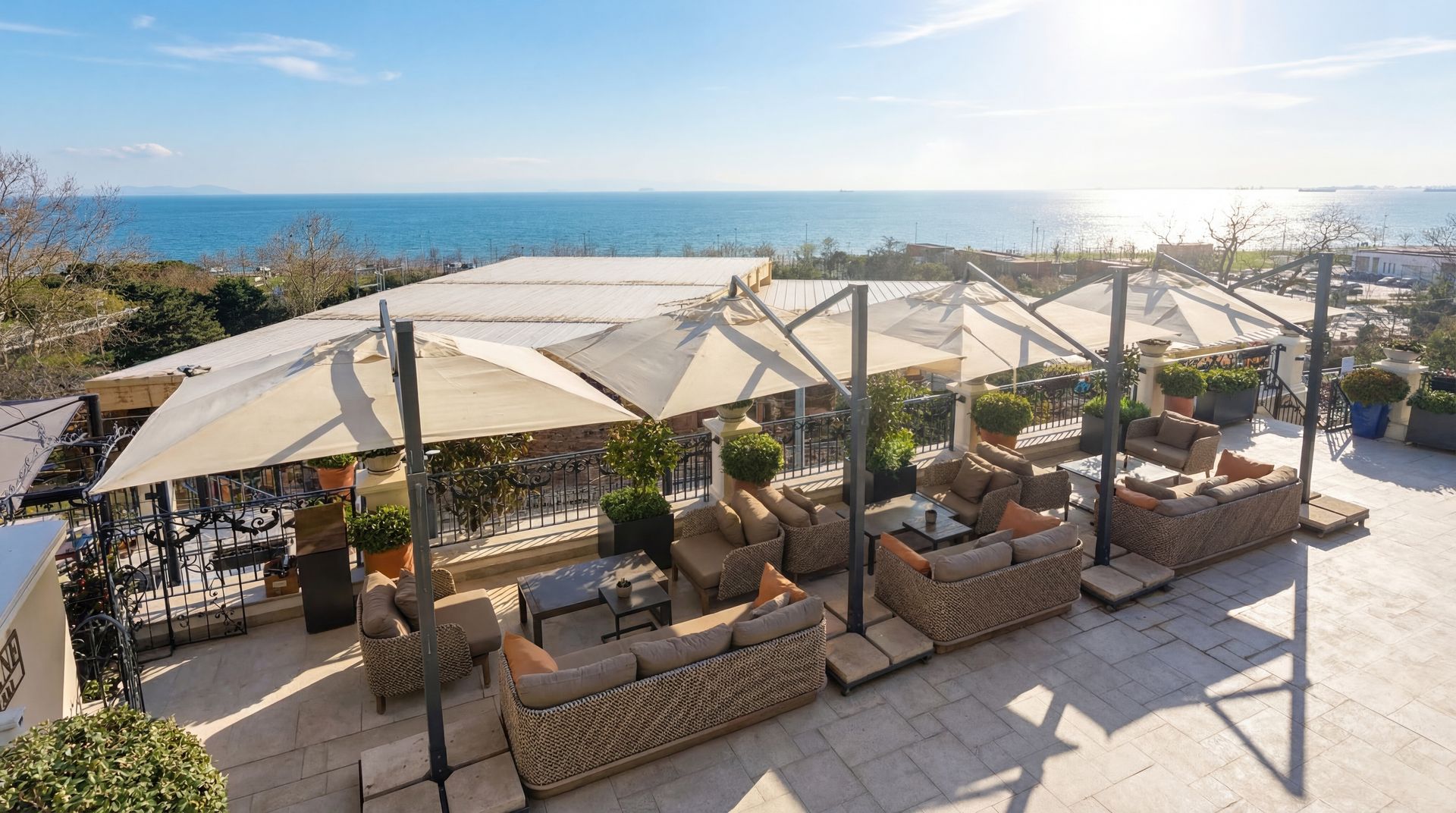 Sunny rooftop lounge with beige umbrellas, outdoor sofas, and ocean view at sunset