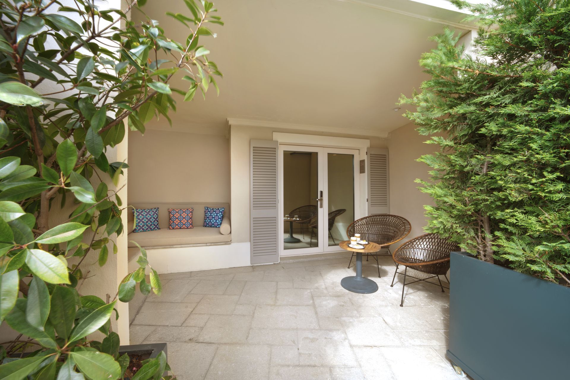 Covered patio with tiled floor, white French doors, potted plants, and wicker chairs