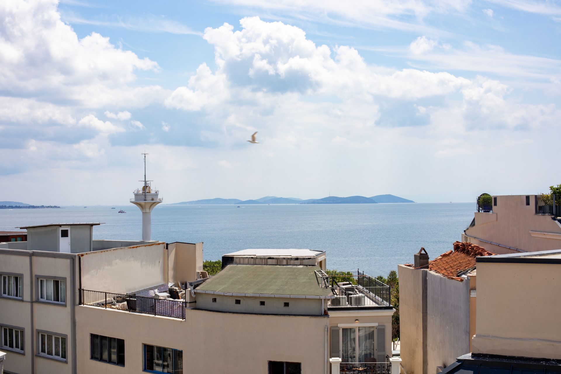 Coastal city rooftops overlooking a blue sea and distant islands under a cloudy sky