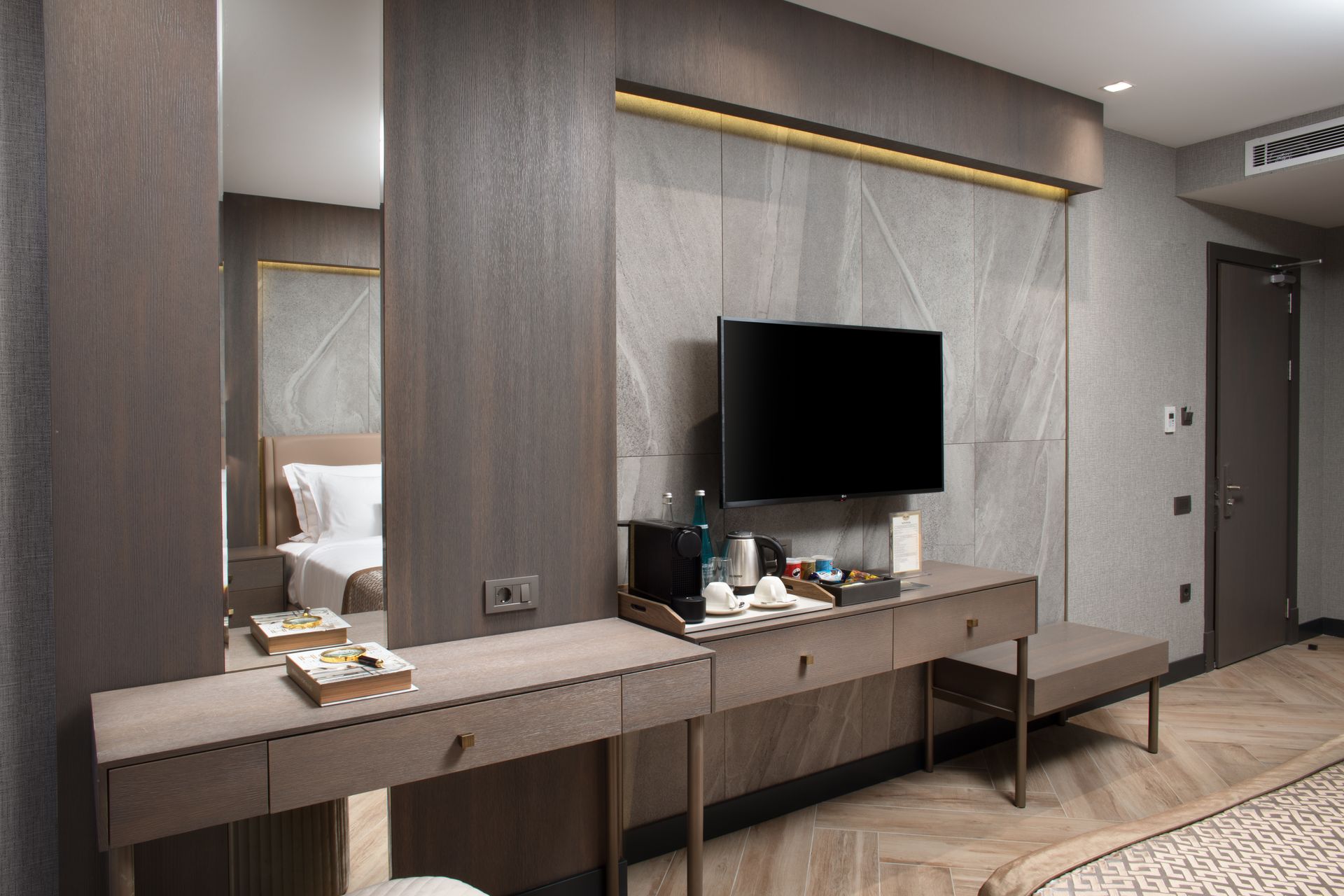 Modern hotel room desk with mirror, TV, chair, and neutral gray decor