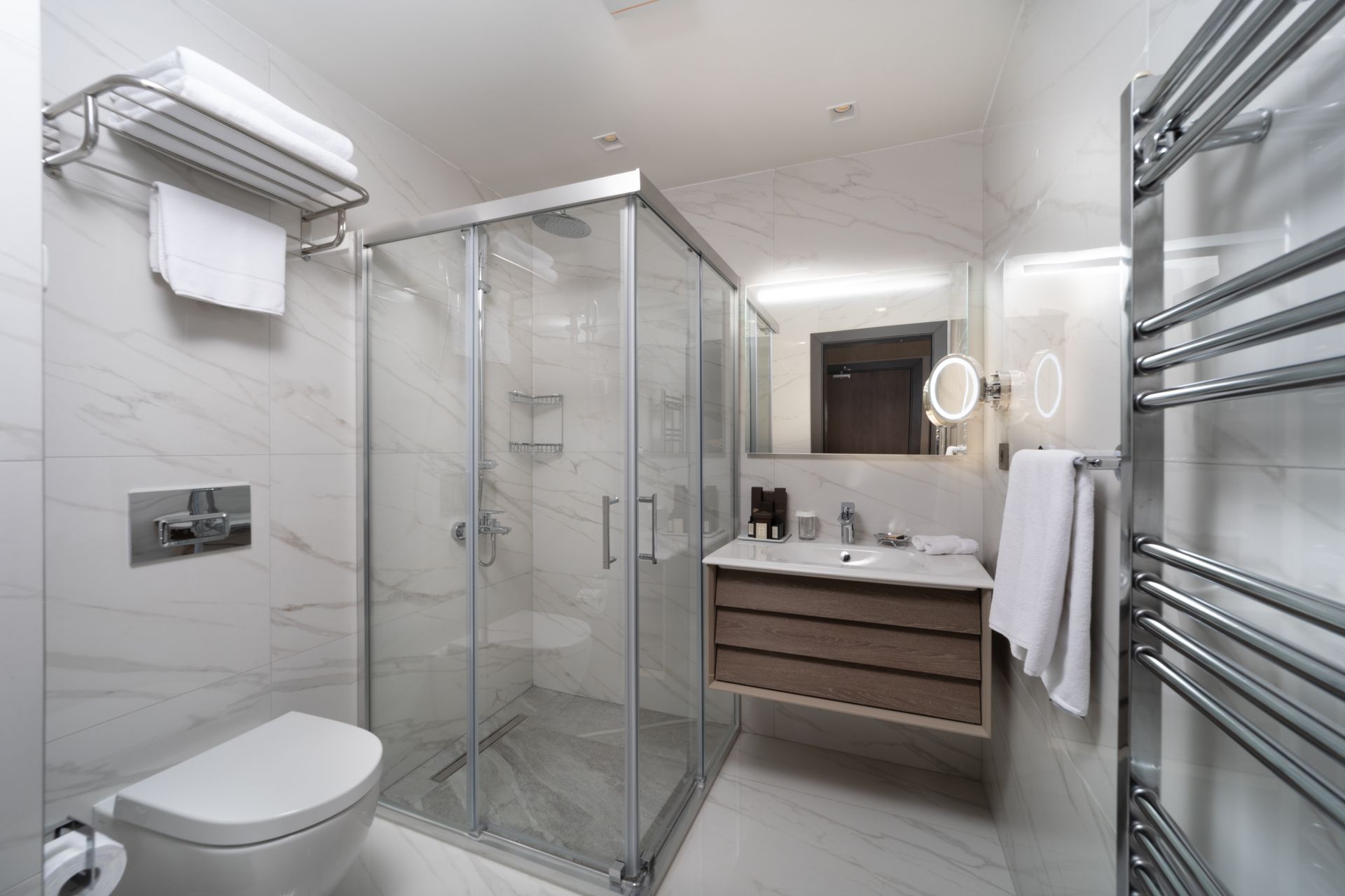 Modern white bathroom with glass shower, vanity, toilet, and towel warmers