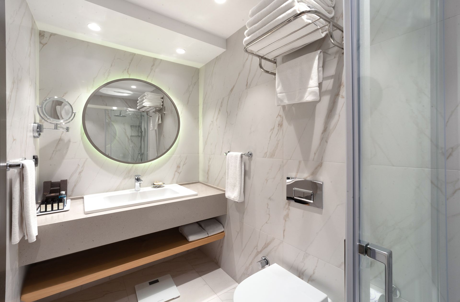Modern bathroom with floating sink, round mirror, glass shower, and white towels