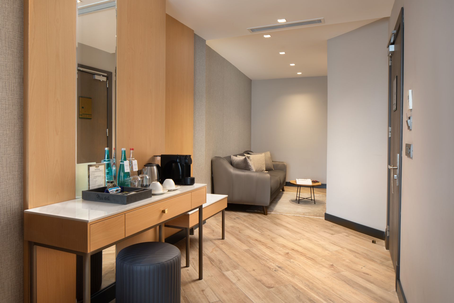 Modern hotel room with a vanity, bed, armchair, and warm wood flooring.