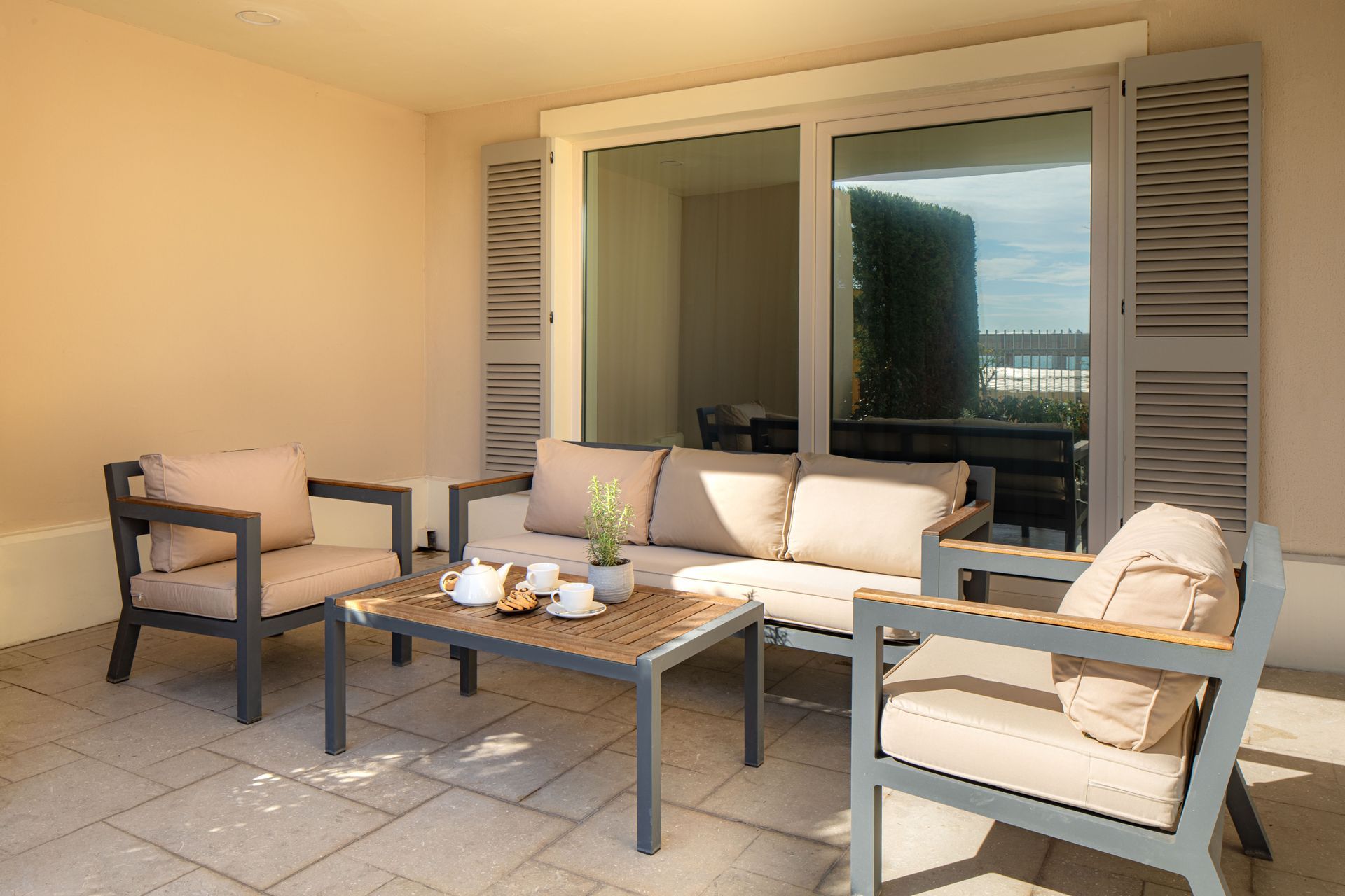 Outdoor patio with cream cushioned chairs, coffee table, and open sliding doors to a home interior